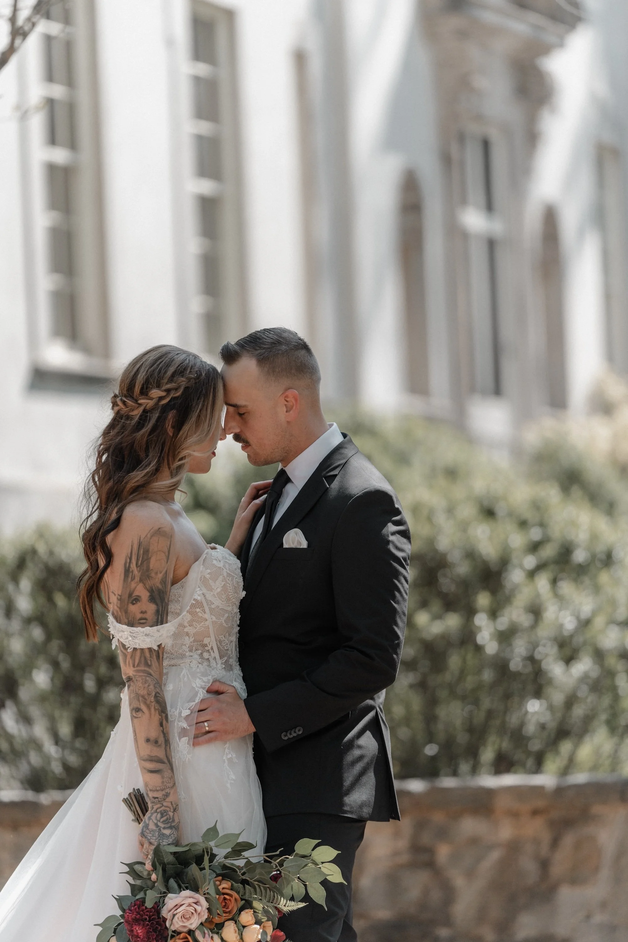 An intimate embrace between a bride and groom, framed by classic stone architecture, captured with timeless elegance