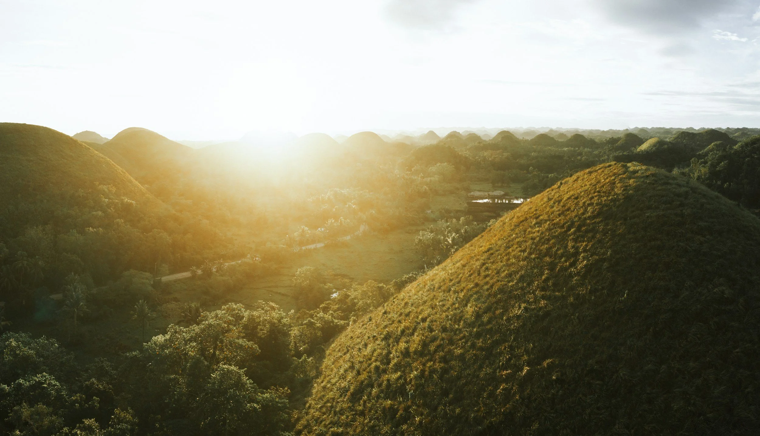Rolling hills stretch into the distance under low sun, layered terrain unfolding quietly within a cinematic prenup film wide frame.