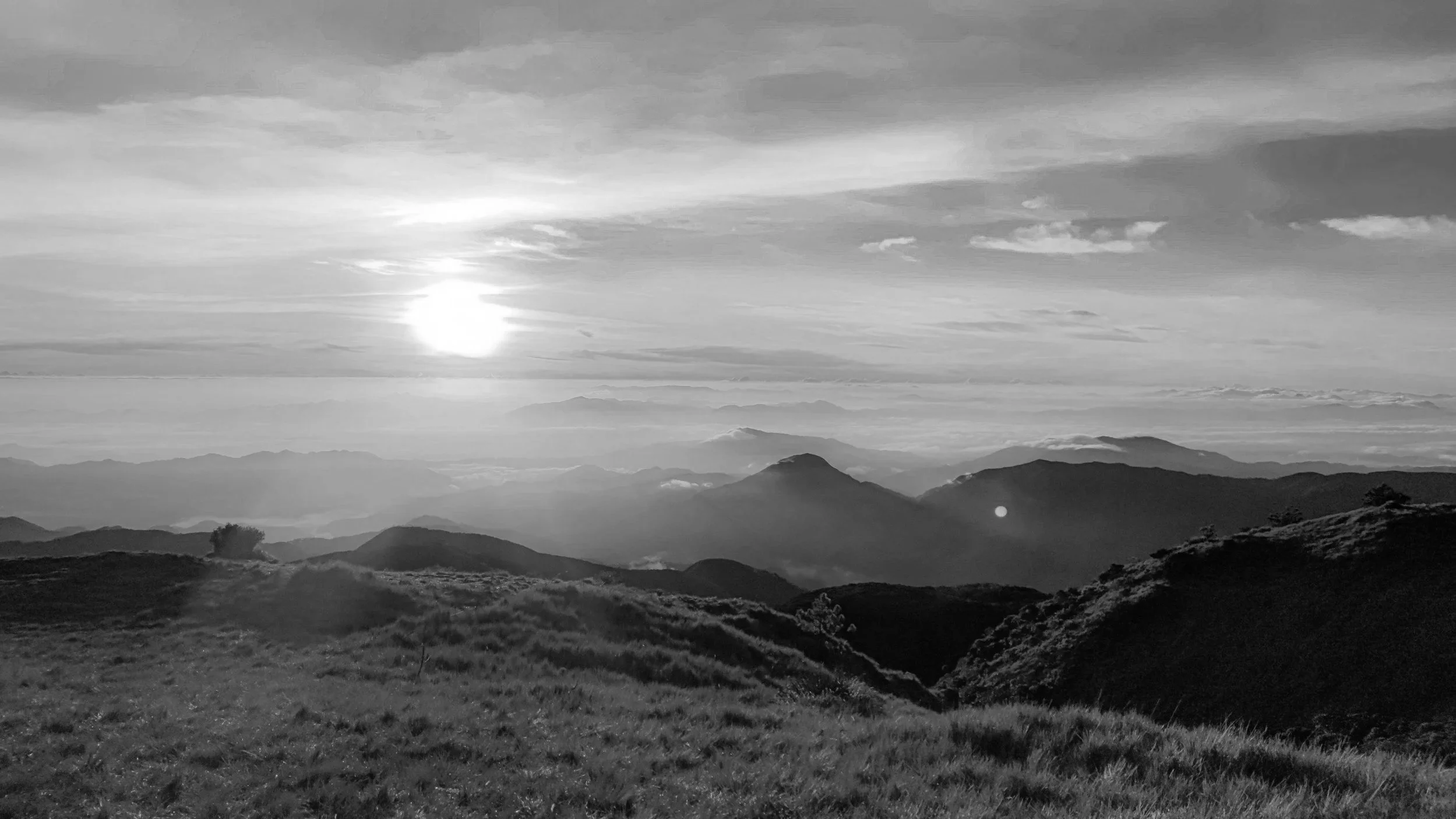 The sun hovers above distant mountain ridges as light fades across the landscape, filmed as a wide cinematic prenup film sequence.
