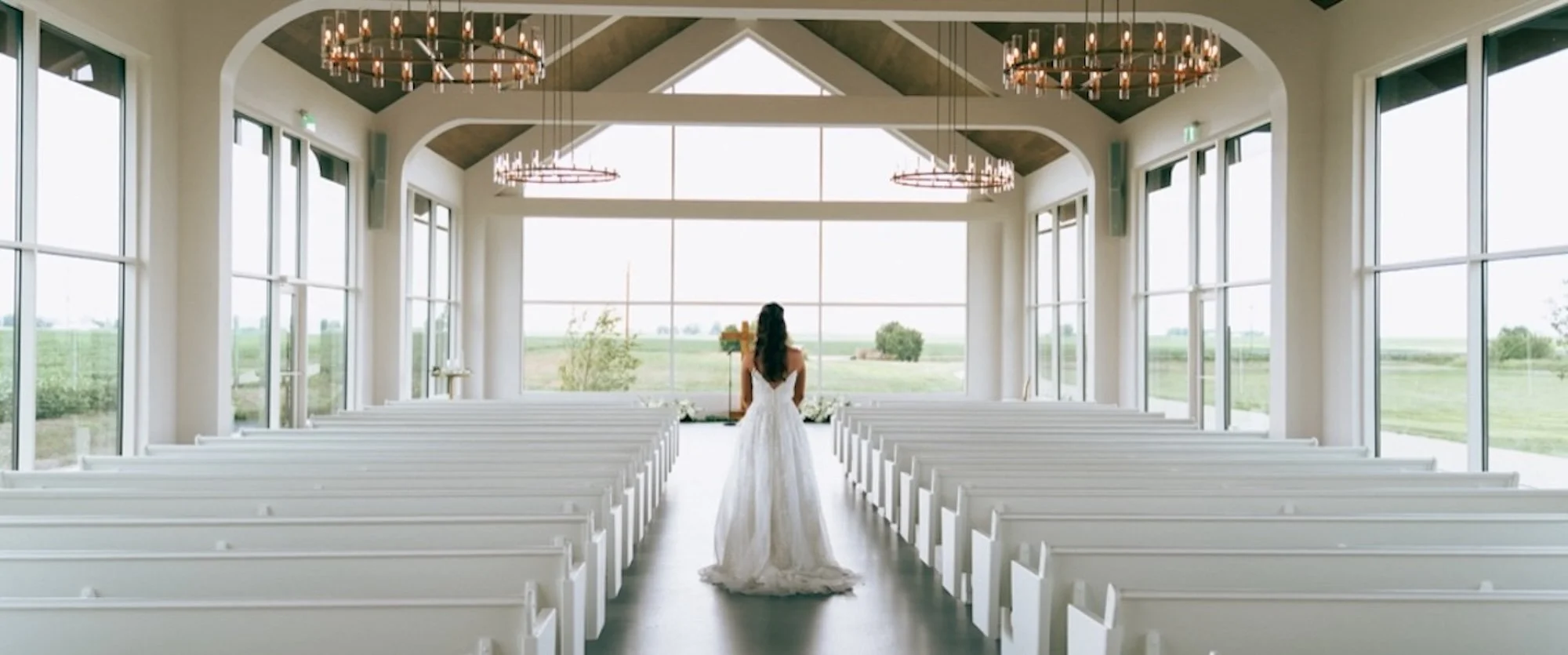 Bride walks alone through modern white chapel aisle, framed by glowing light