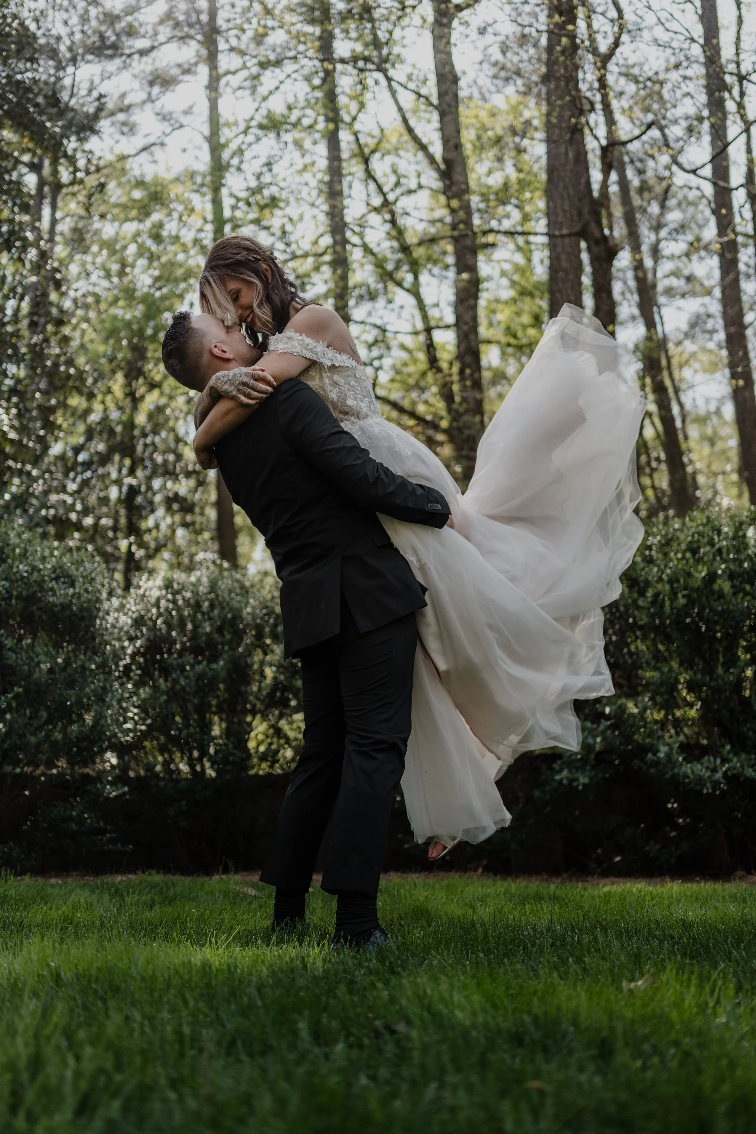 A groom lifts his bride into the air, her gown flowing as they share a moment of pure joy, captured with cinematic elegance.
