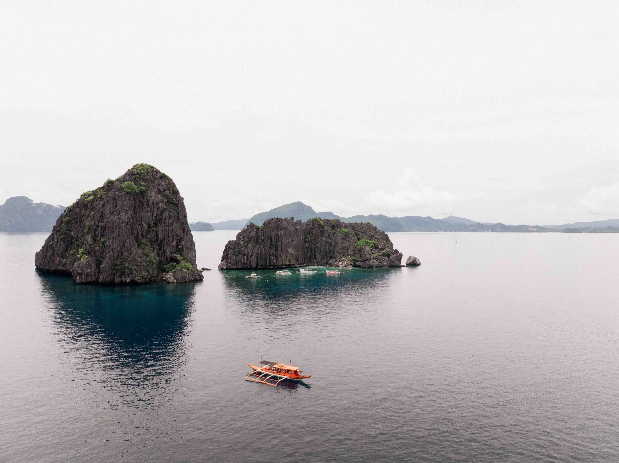 Boat drifts through turquoise water surrounded by limestone cliffs, horizon wide and still