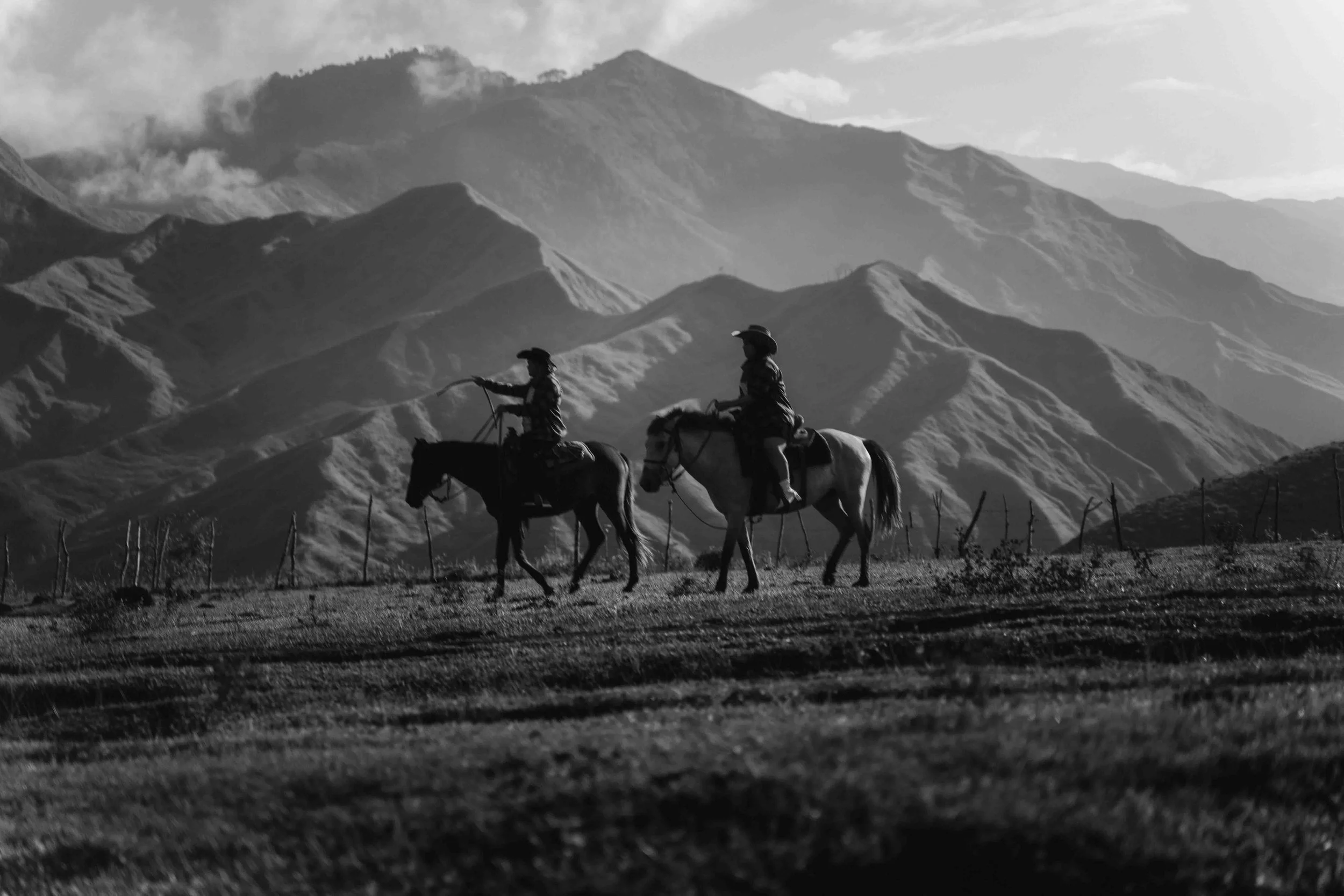 Two riders move across an open landscape on horseback, silhouettes layered against distant mountains and textured ground in Bukidnon.
