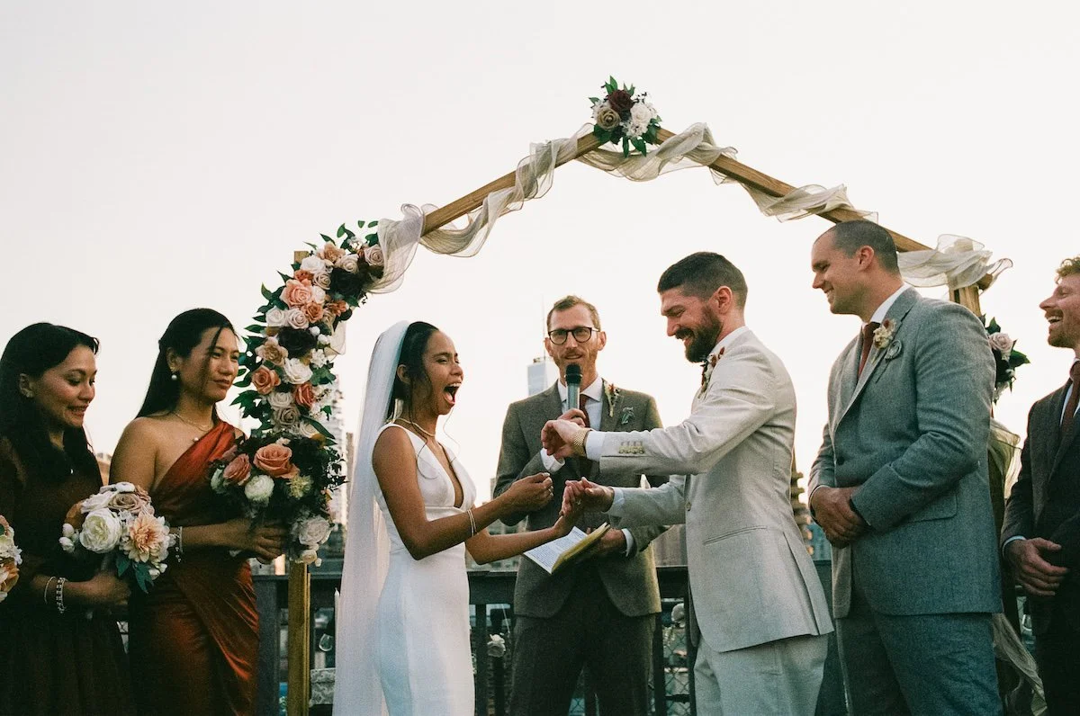 Bride laughing as she exchanges vows with the groom under a floral arch, ceremony moment inspired by New York City weddings captured by Caz Isaiah