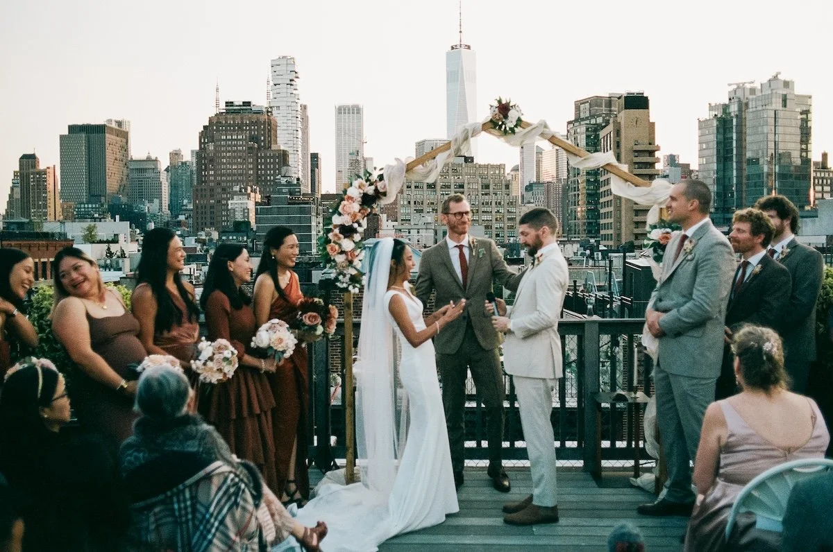 620 Loft & Garden Wedding Photographer — couple exchanging vows in front of family and friends, framed by the city skyline.