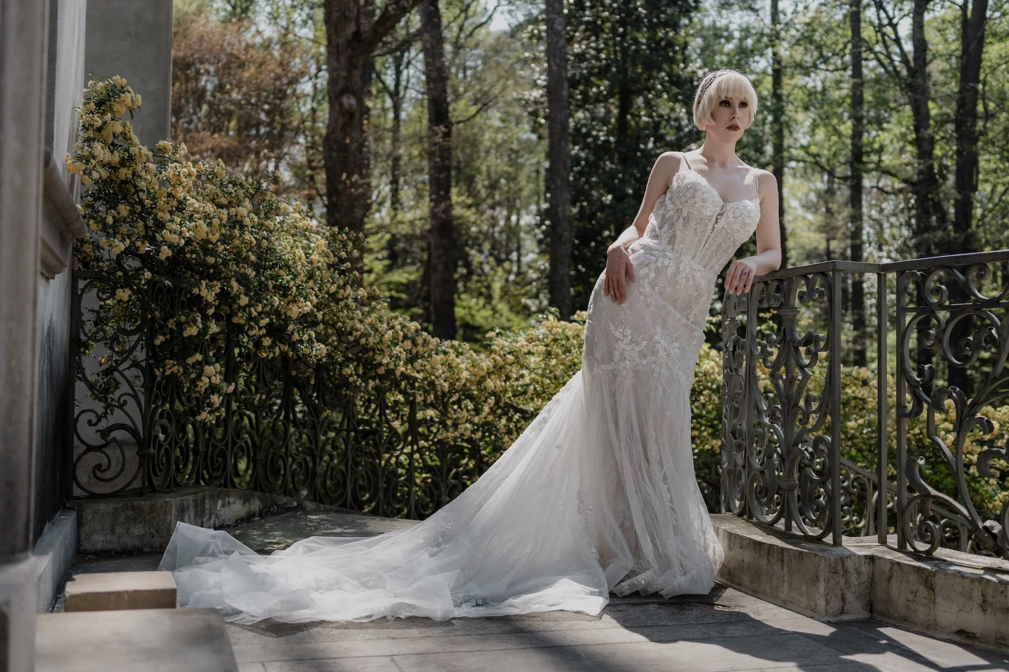 A bride leans gracefully against stone railings in a lace gown, framed in a Kyoto inspired wedding setting of natural greenery and quiet light.