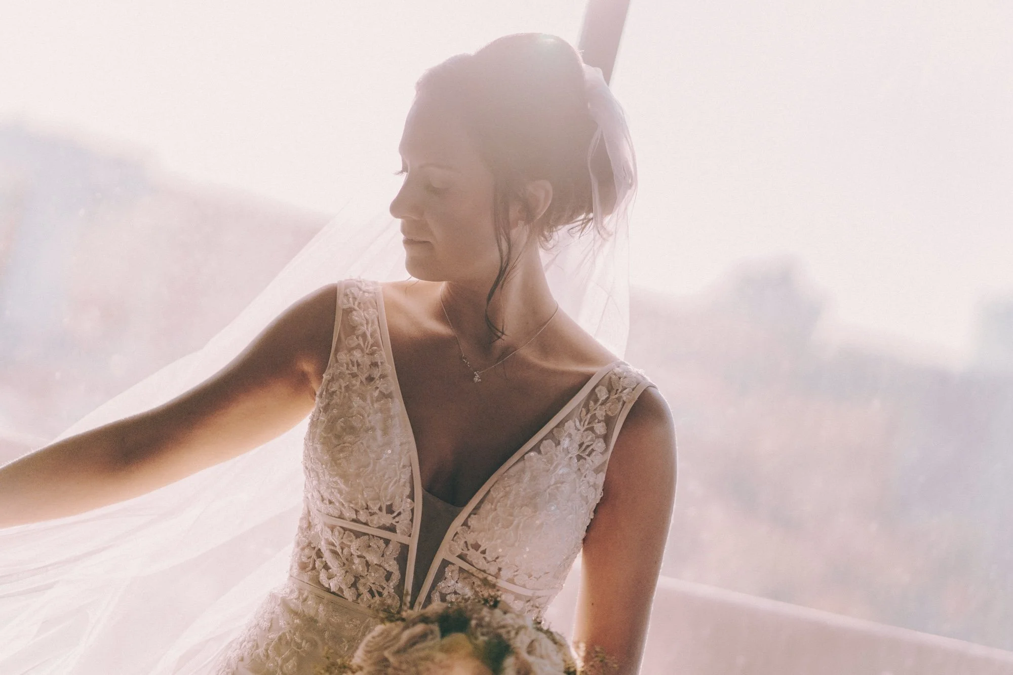 A bride lifting her arm gracefully, sunlight spilling across her dress, cinematic and delicate.