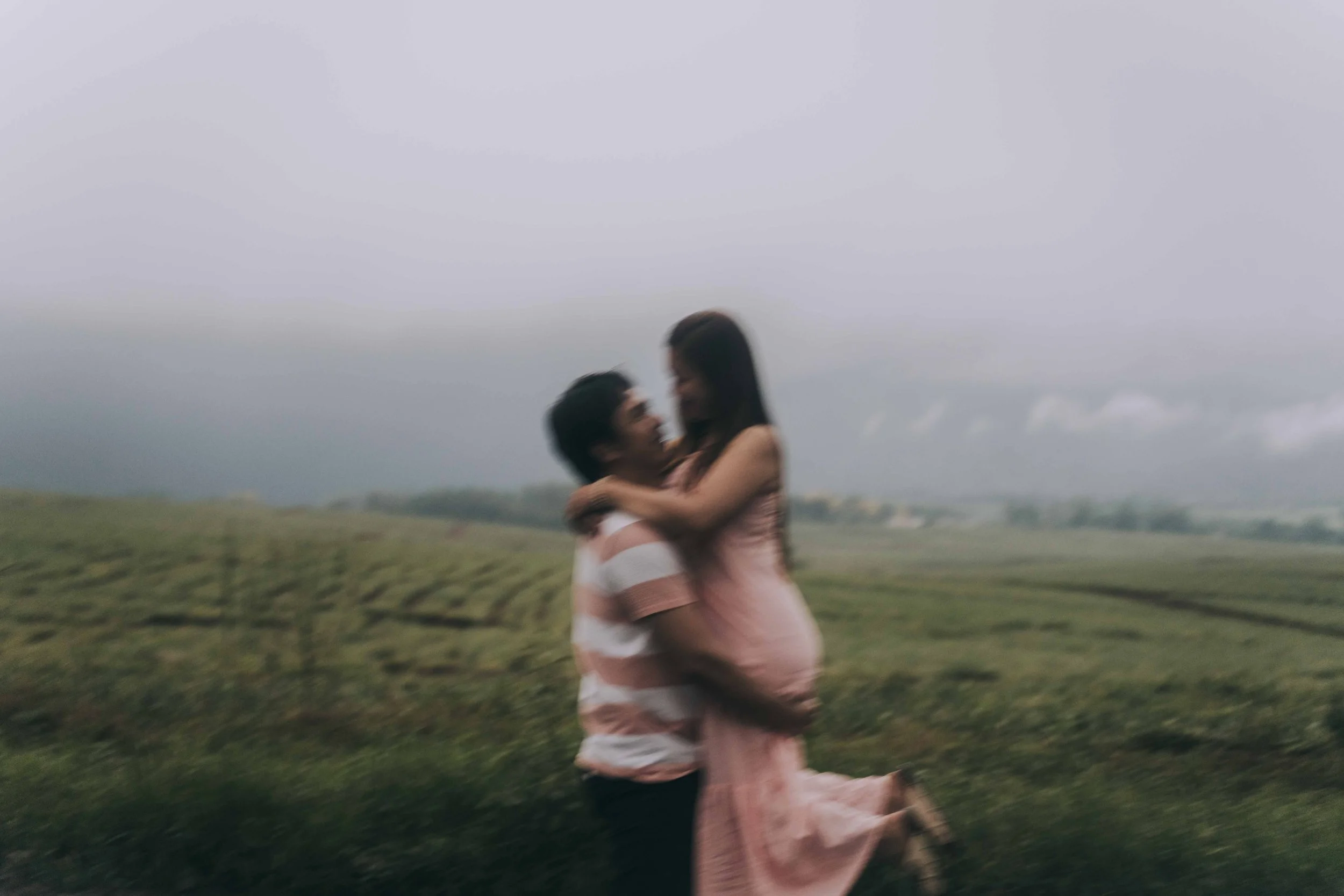 One partner lifts the other while standing in an open field, bodies slightly blurred by motion and distance.
