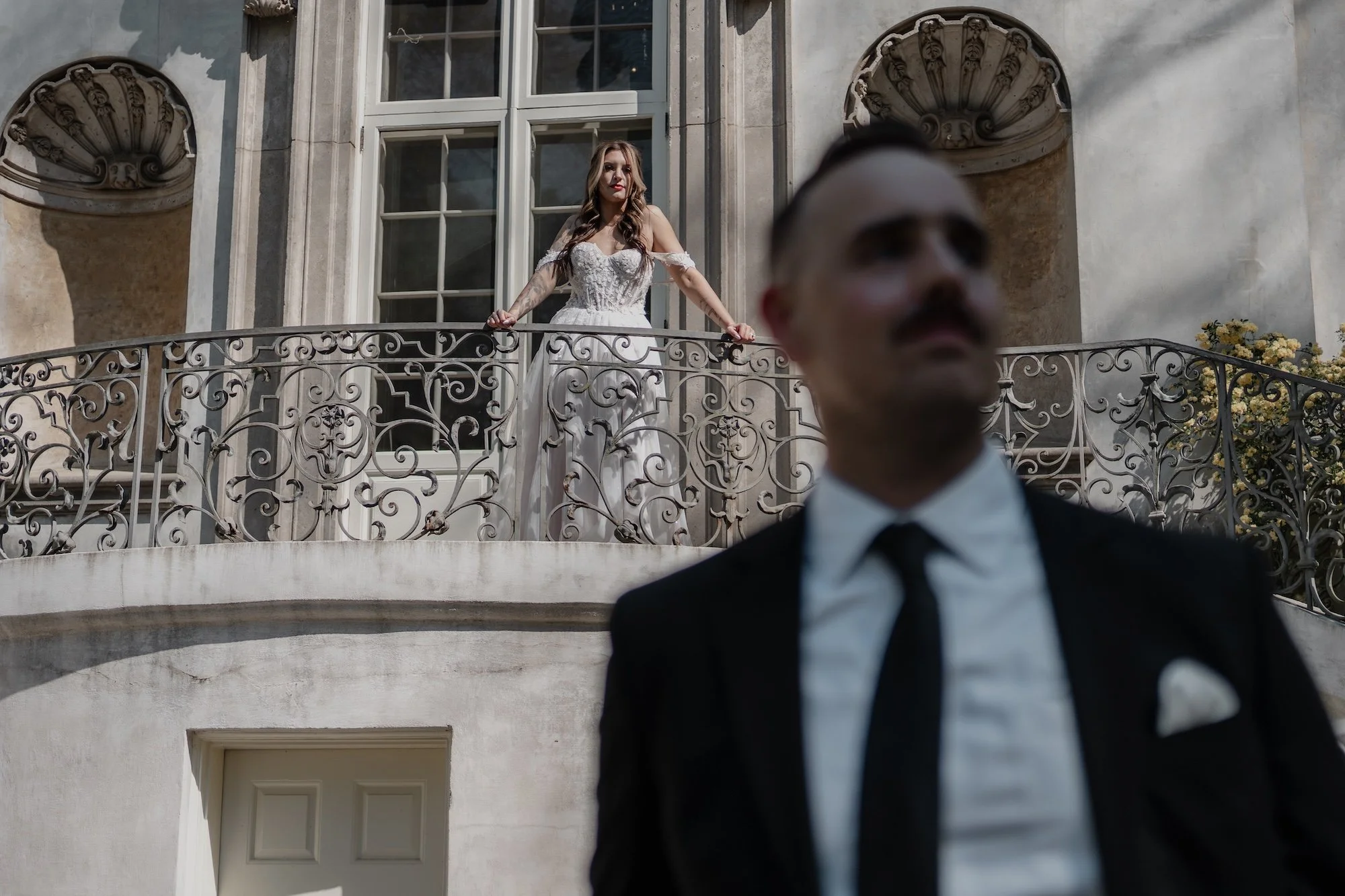 Groom in suit with bride standing above on balcony, cinematic perspective of a wedding day