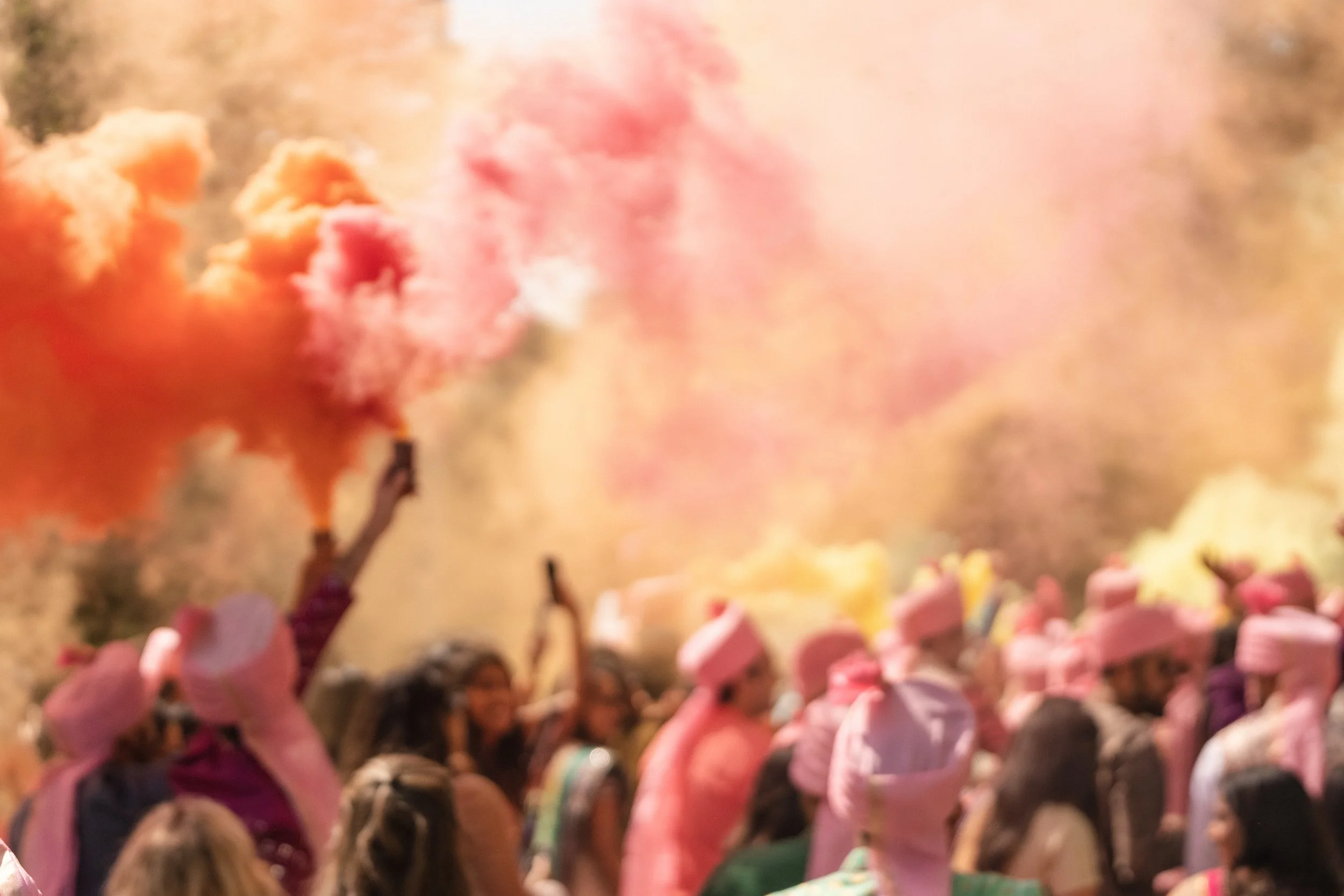 Vibrant clouds of color fill the sky as guests celebrate together during a wedding procession, cinematic energy captured by Caz Isaiah