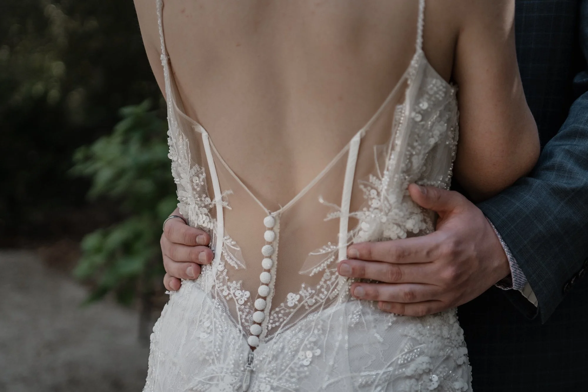 The back of a gown held gently, lace textures captured with quiet detail.