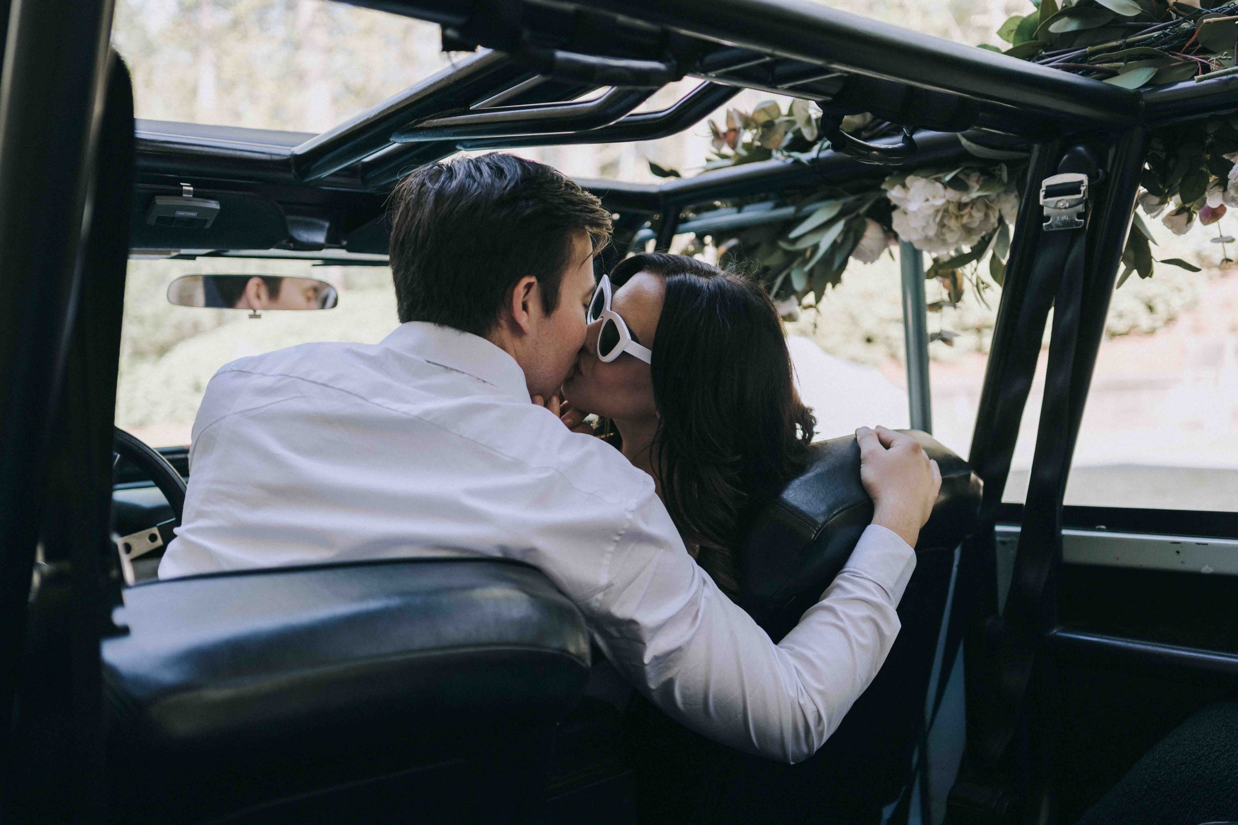 Couple sharing a kiss in an open-top jeep decorated with flowers — captured by Alila Villas Uluwatu Wedding Photographer.