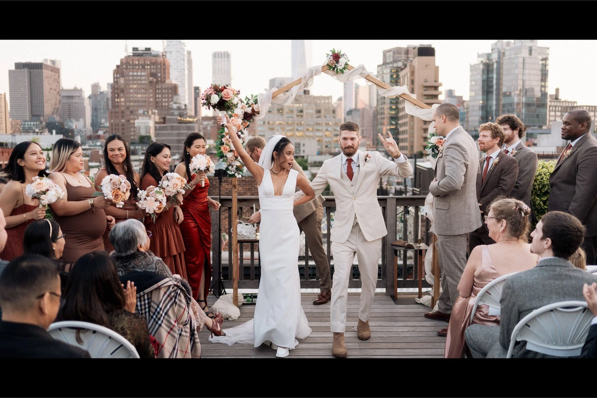 A couple celebrates their ceremony outdoors surrounded by guests and city skyline, hands raised in joy, inspired by Viceroy Bali weddings
in NYC