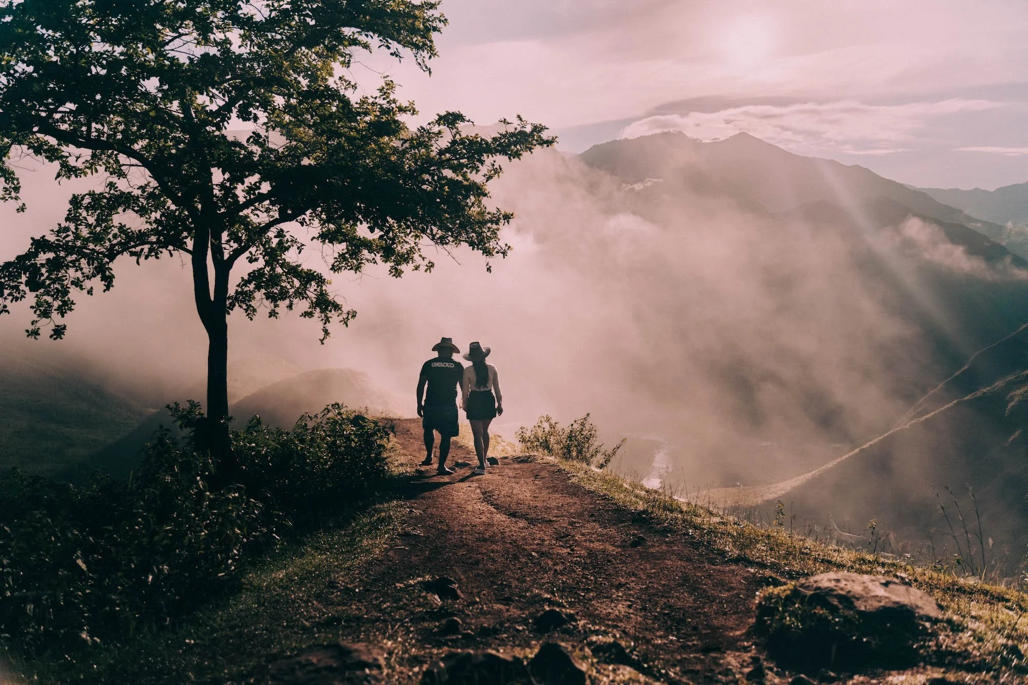 Two figures walk a ridgeline as mist rises, evoking the quiet storytelling of an Uluwatu wedding photographer.