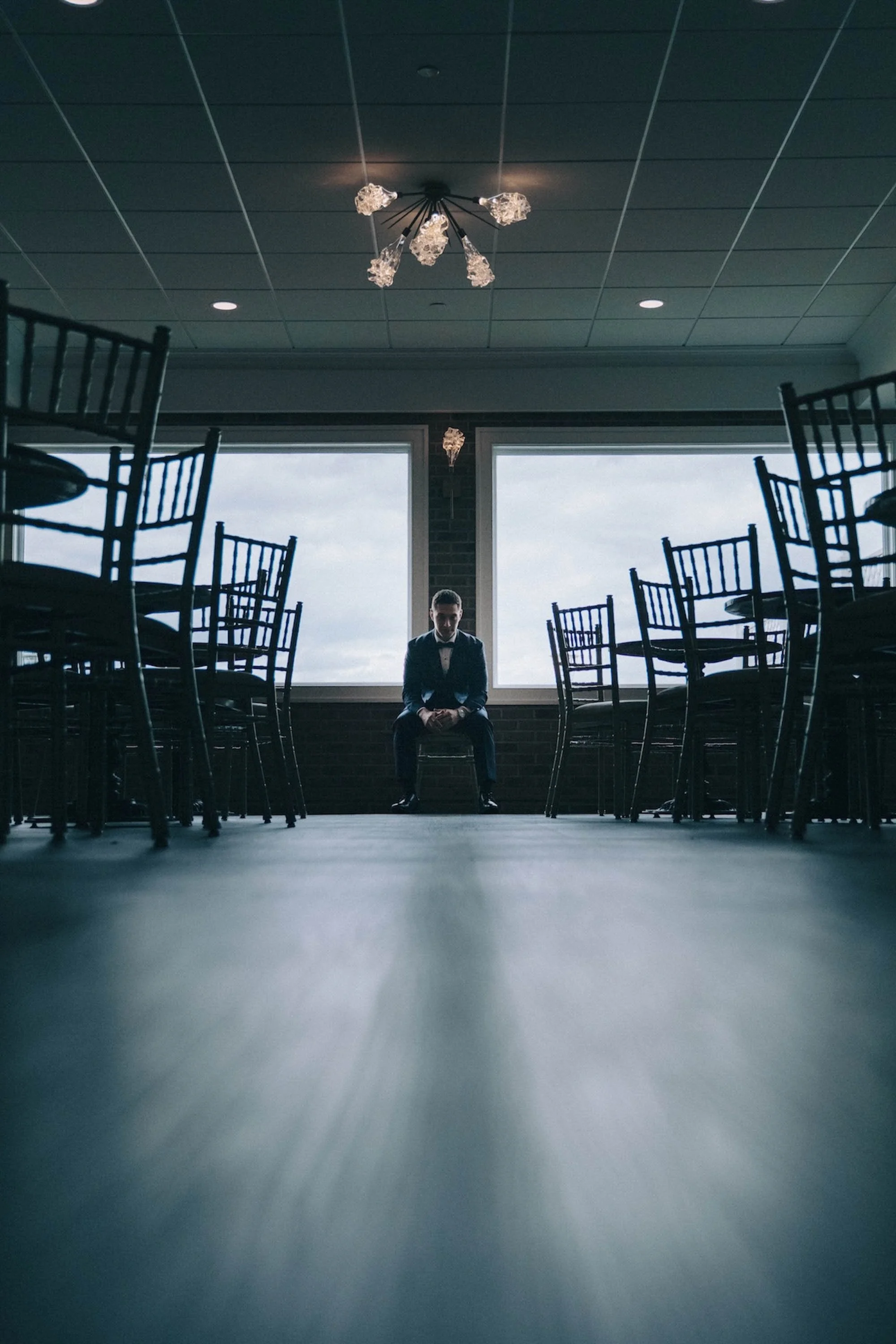 Groom seated alone between rows of empty chairs, a quiet reflective moment