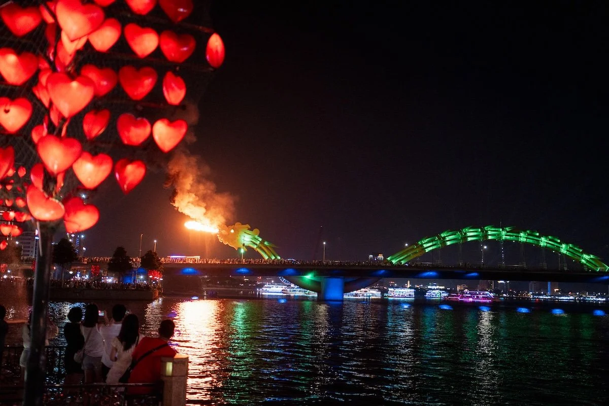 Lanterns glowing red over a night market, flames and bridges lighting the background from the Dragon Bridge in Da Nang