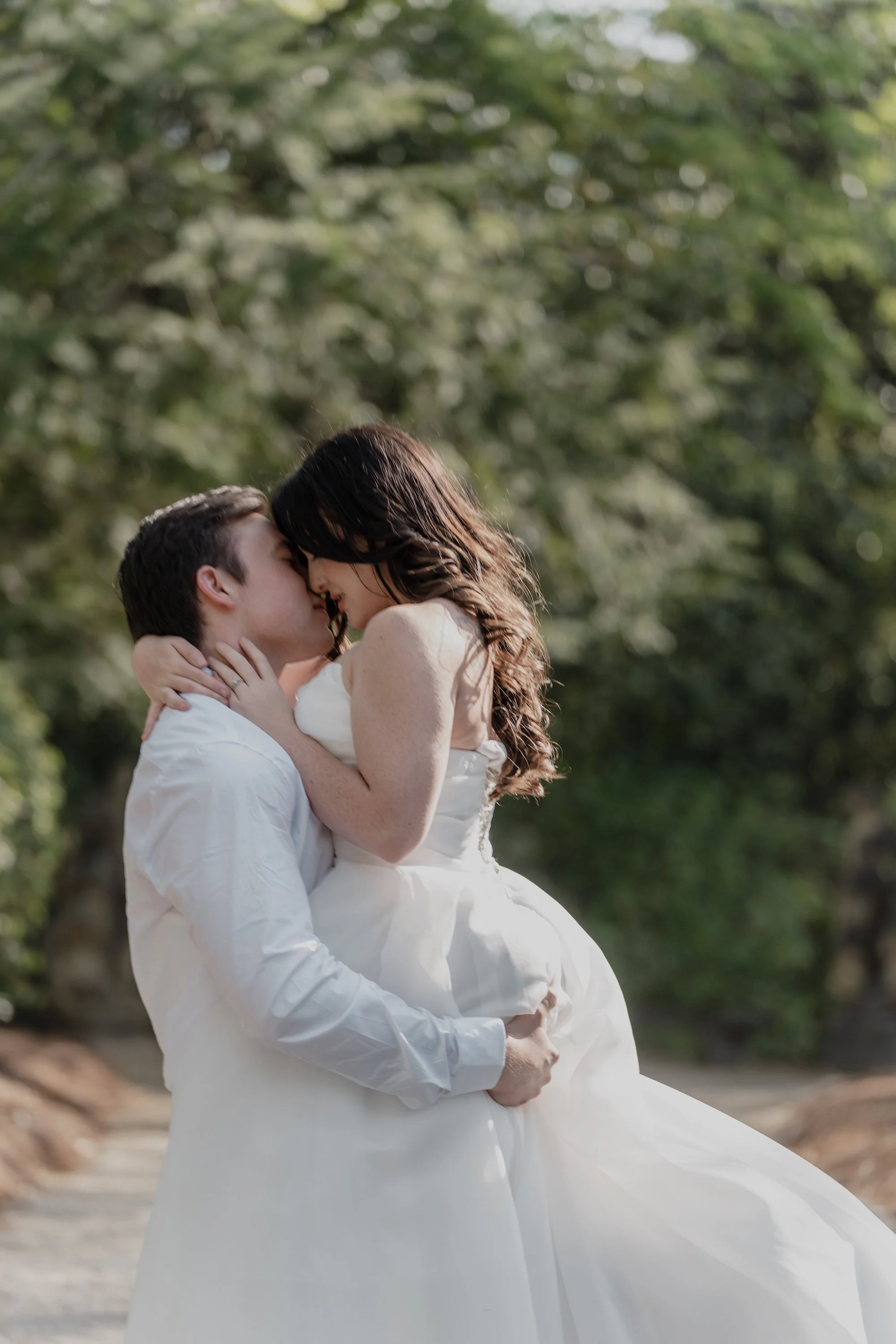 A groom lifting his bride in a soft kiss, wrapped in golden light, the moment held with natural tenderness.