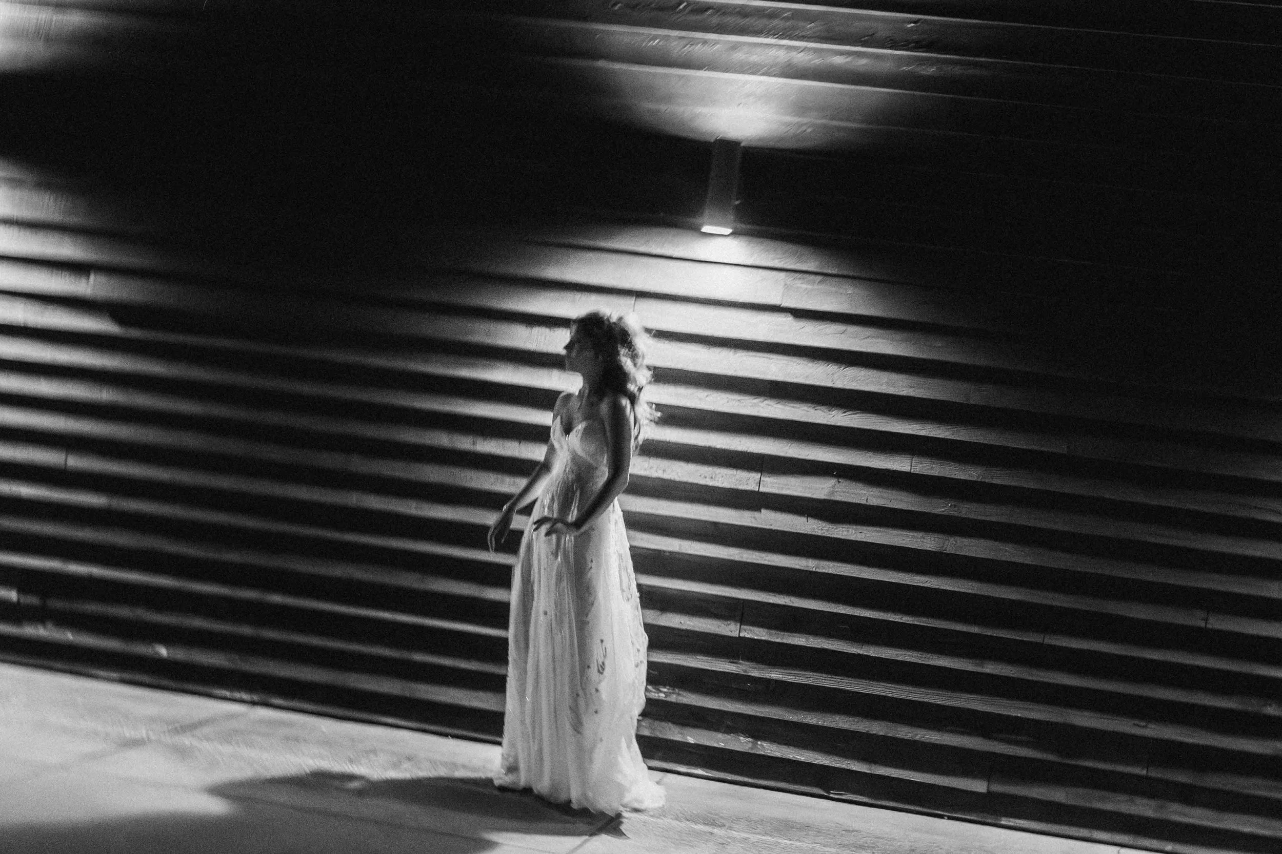 Bride in flowing gown beneath architectural shadows — cinematic portrait by Caz Isaiah inspired by Habitas AlUla’s minimalist desert tones.