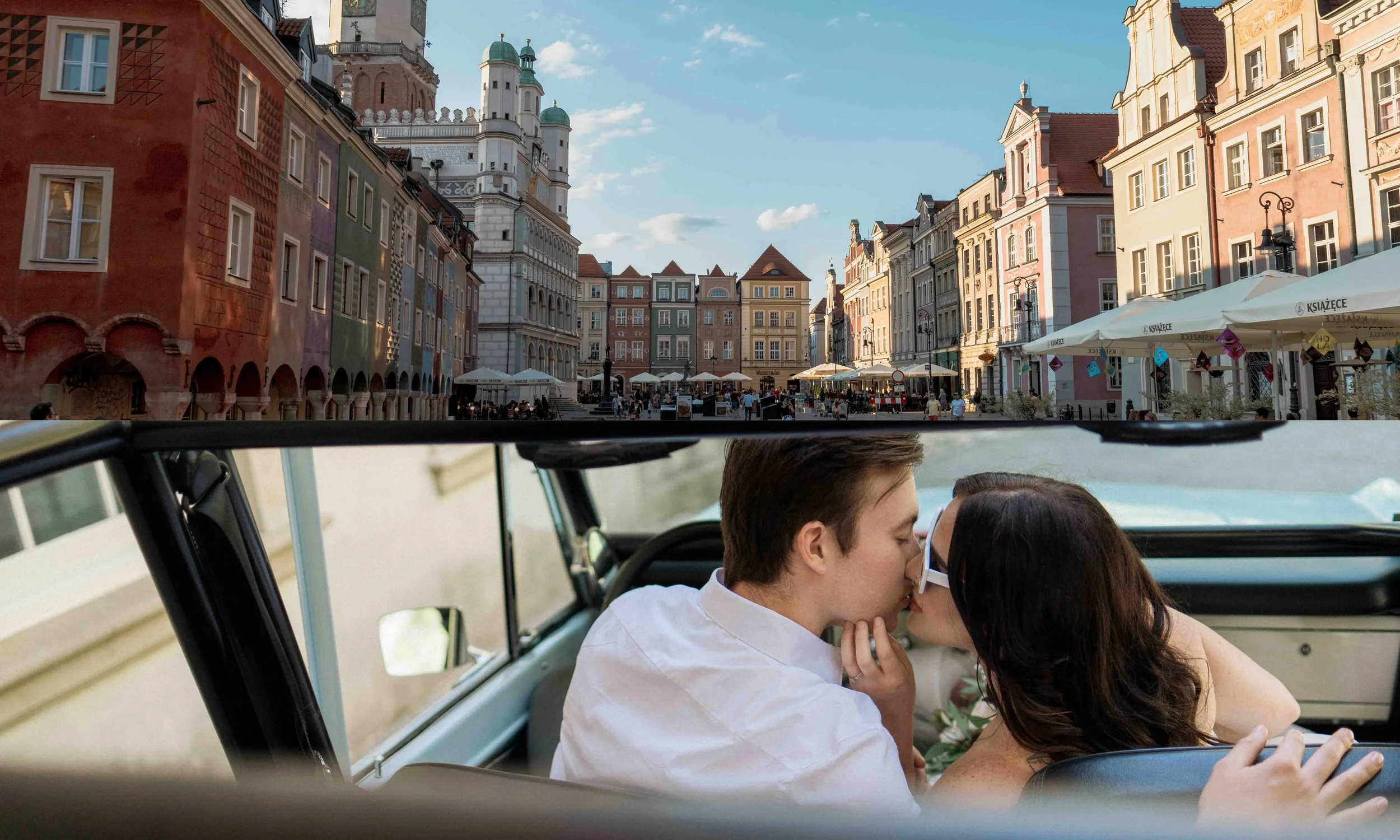 A couple shares a quiet moment inside a vintage car, reflected through glass as they embrace