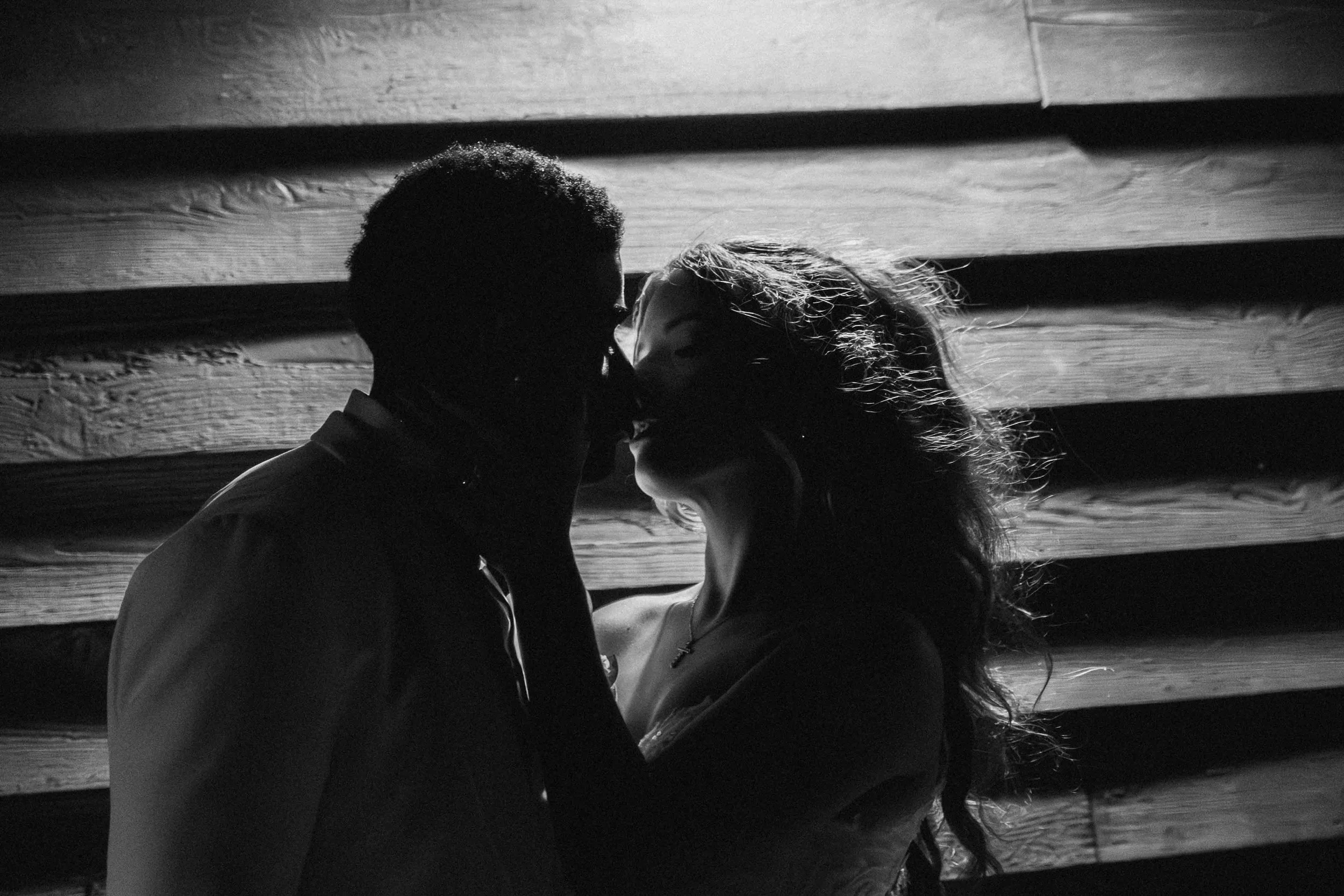A man in formalwear kisses a woman’s forehead near a window, light washing their profiles as a Fragmented Memories couples photographer observes.