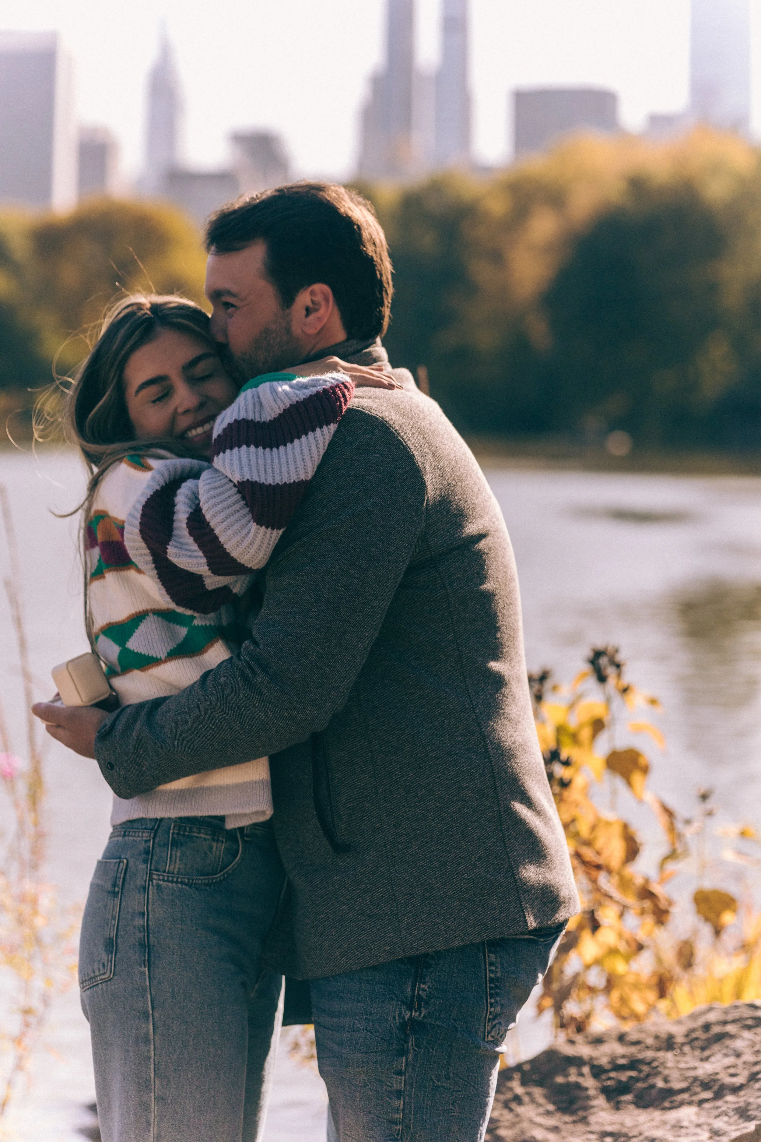 Engagement moment in Central Park, with skyline views and autumn colors by the lake.