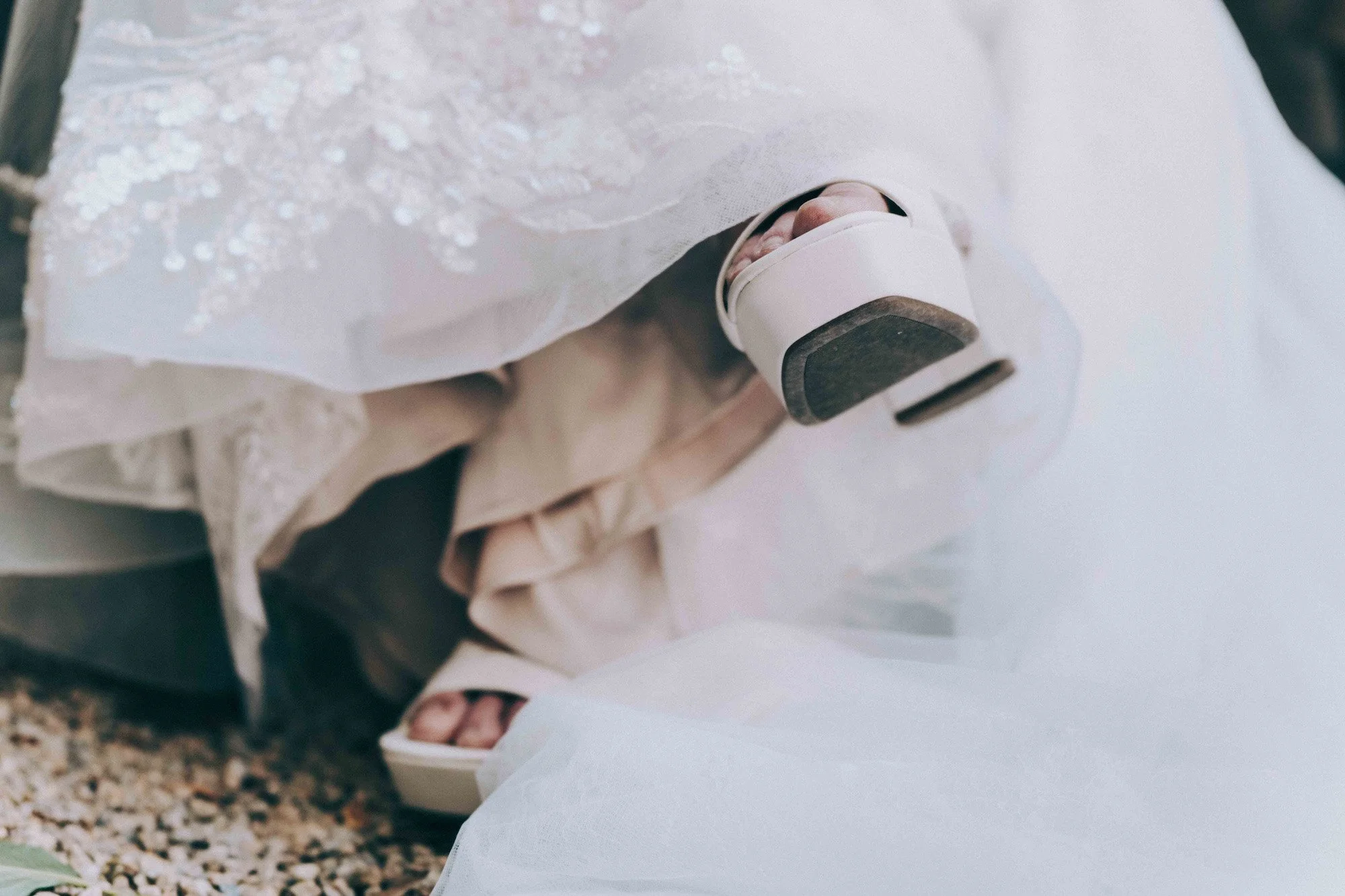 Close-up of bride’s shoes resting beneath her gown, veil and fabric surrounding soft details, captured with cinematic intimacy