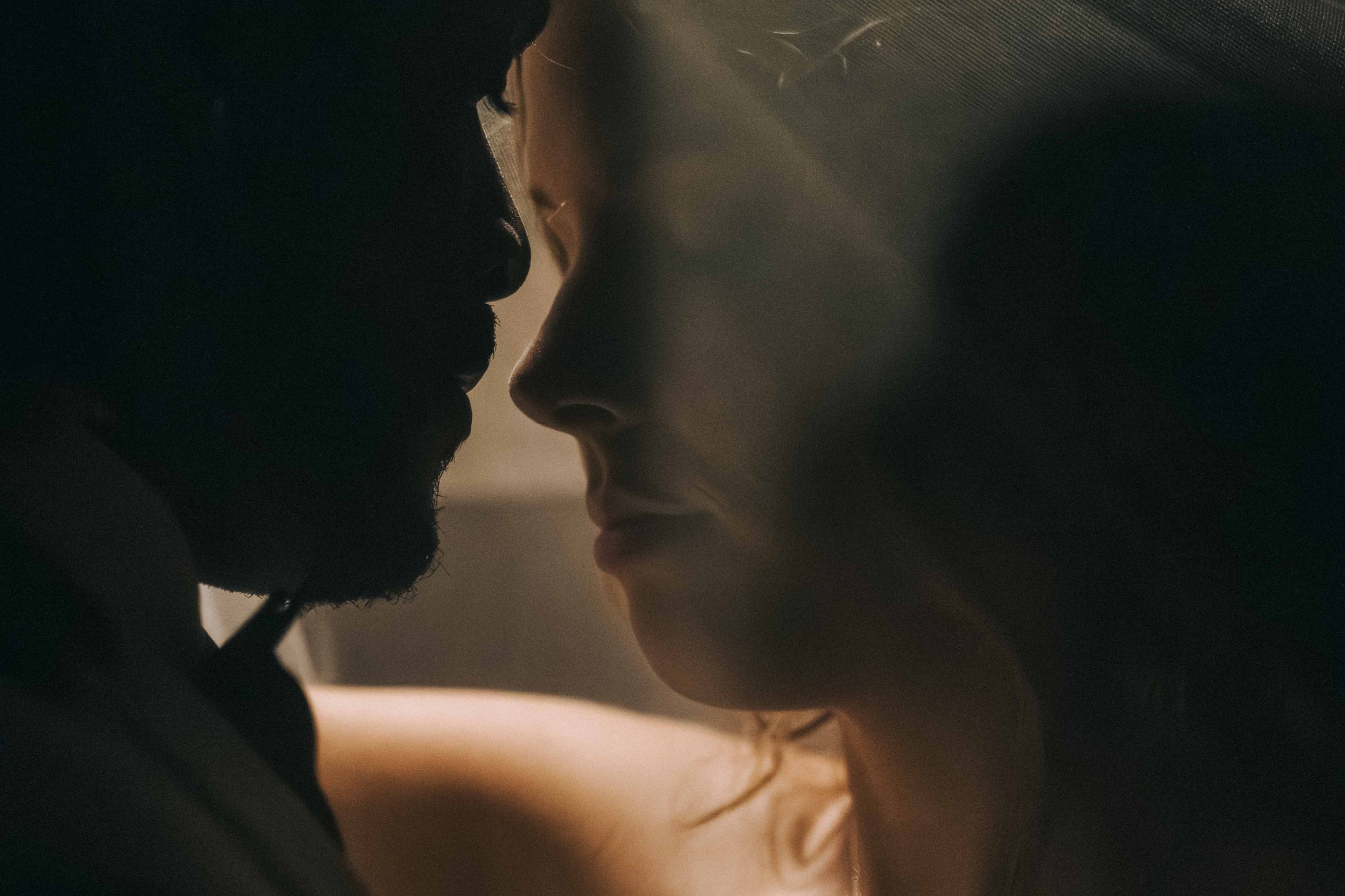 Two faces meet in profile indoors, noses nearly touching as soft light falls across their skin in a Fragmented Memories prenup photographer scene.