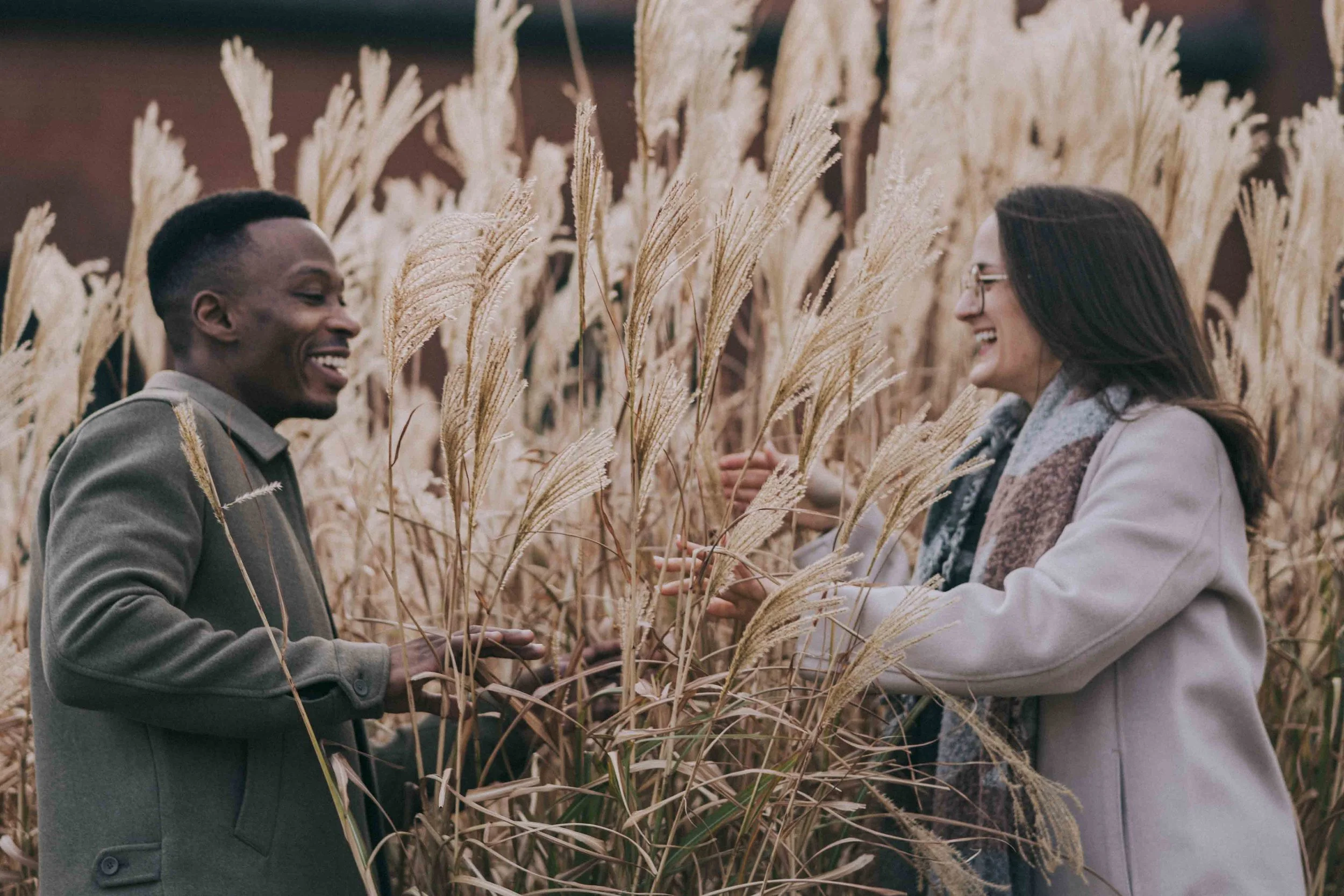 A couple moves through tall dry grass, hands brushing stems as Fragmented Memories prenup photographer observes their shared pace and direction.
