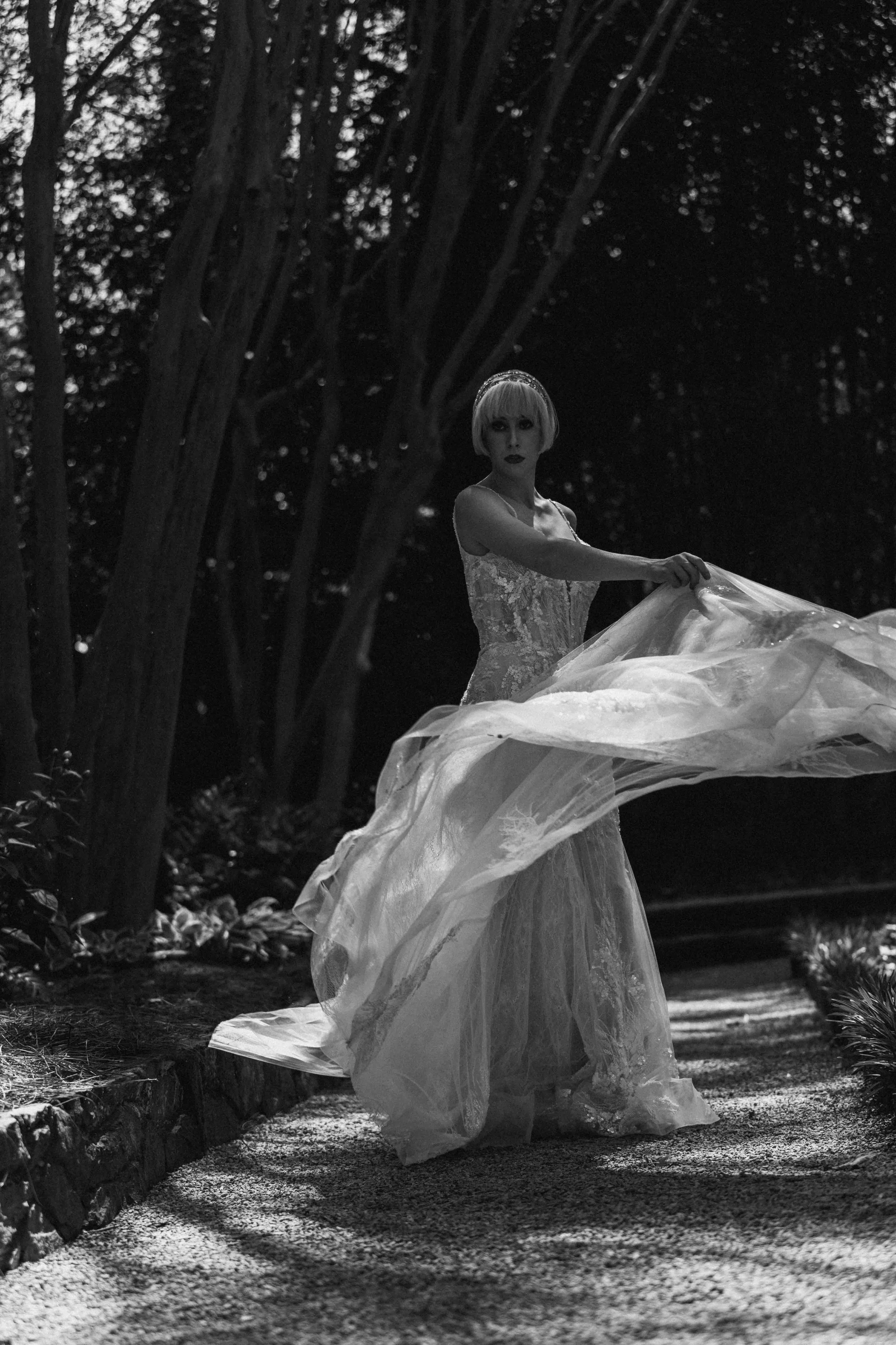 Bride lifts her gown in a garden courtyard, sunlight catching the lace as she turns toward the camera — captured by Caz Isaiah.