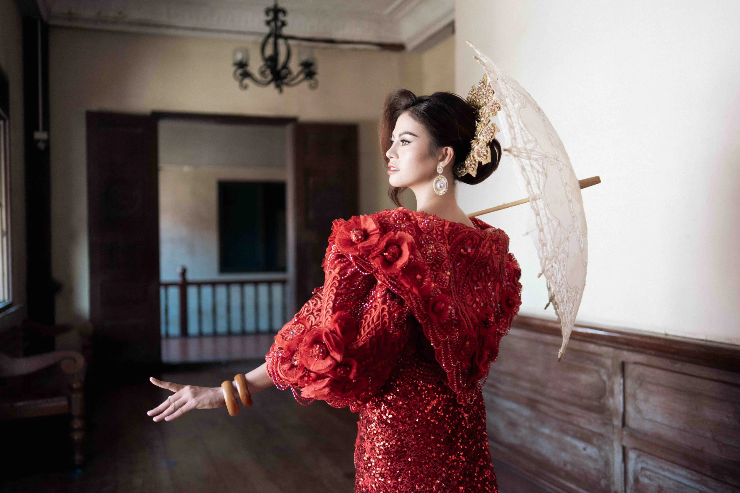 A woman in a red dress holds an umbrella in soft window light, Bali photographer Caz Isaiah captures timeless portrait style