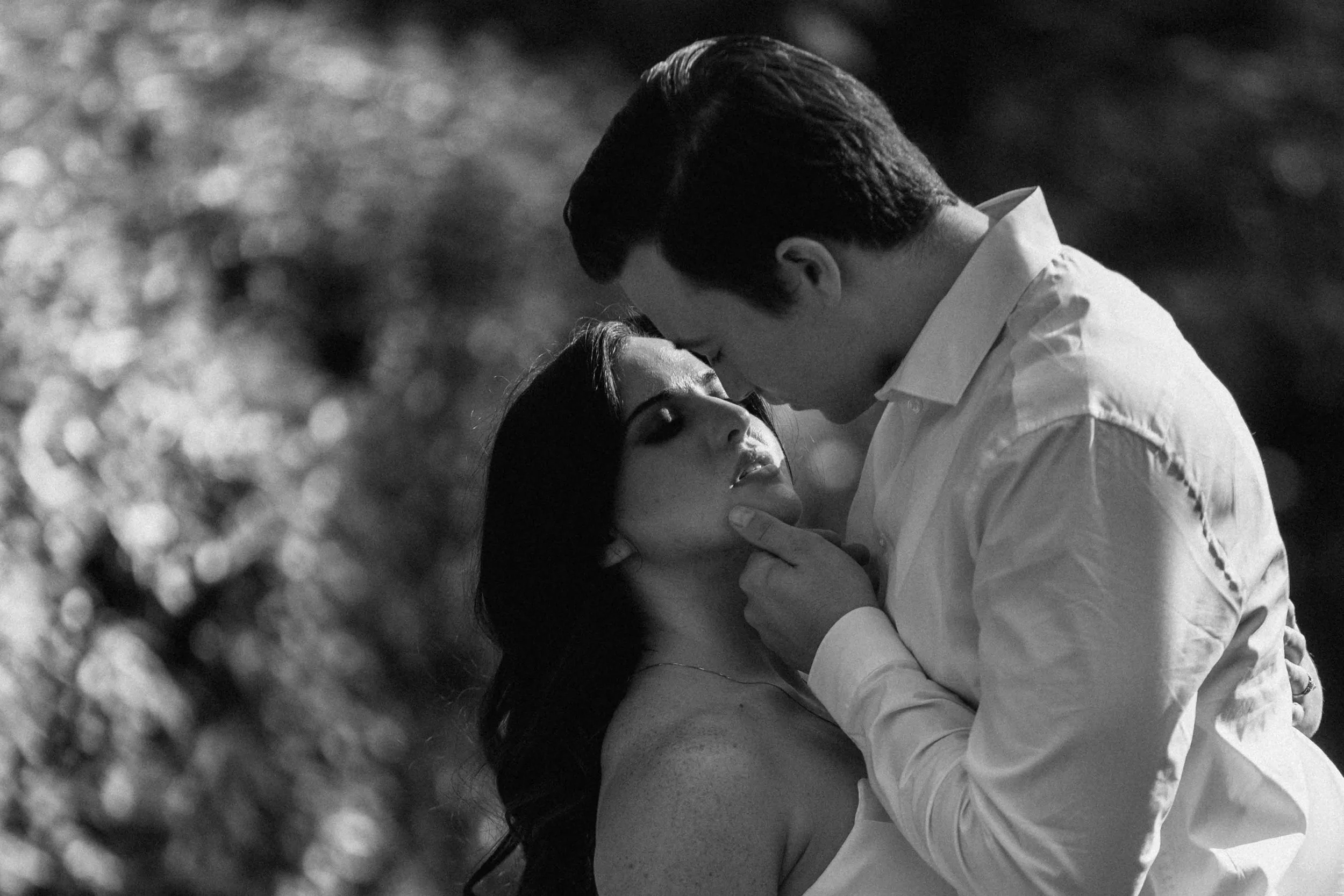 A couple stands face to face, one hand lifting a chin as their bodies draw closer, held in a cinematic prenup film frame.