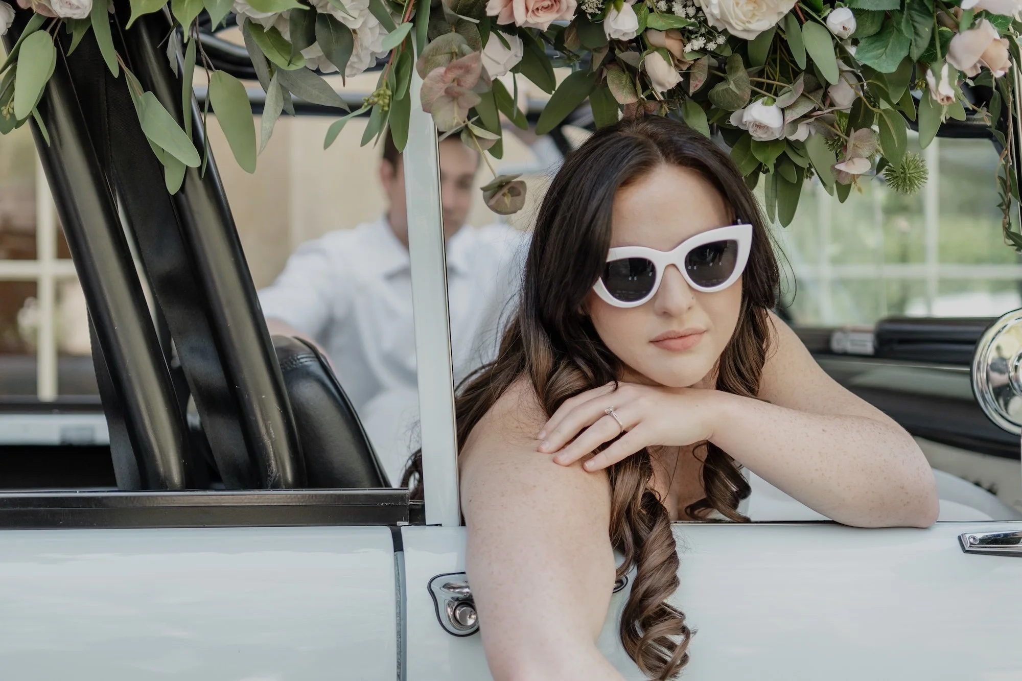 A bride wearing white sunglasses in a car, captured by Caz Isaiah with editorial edge.