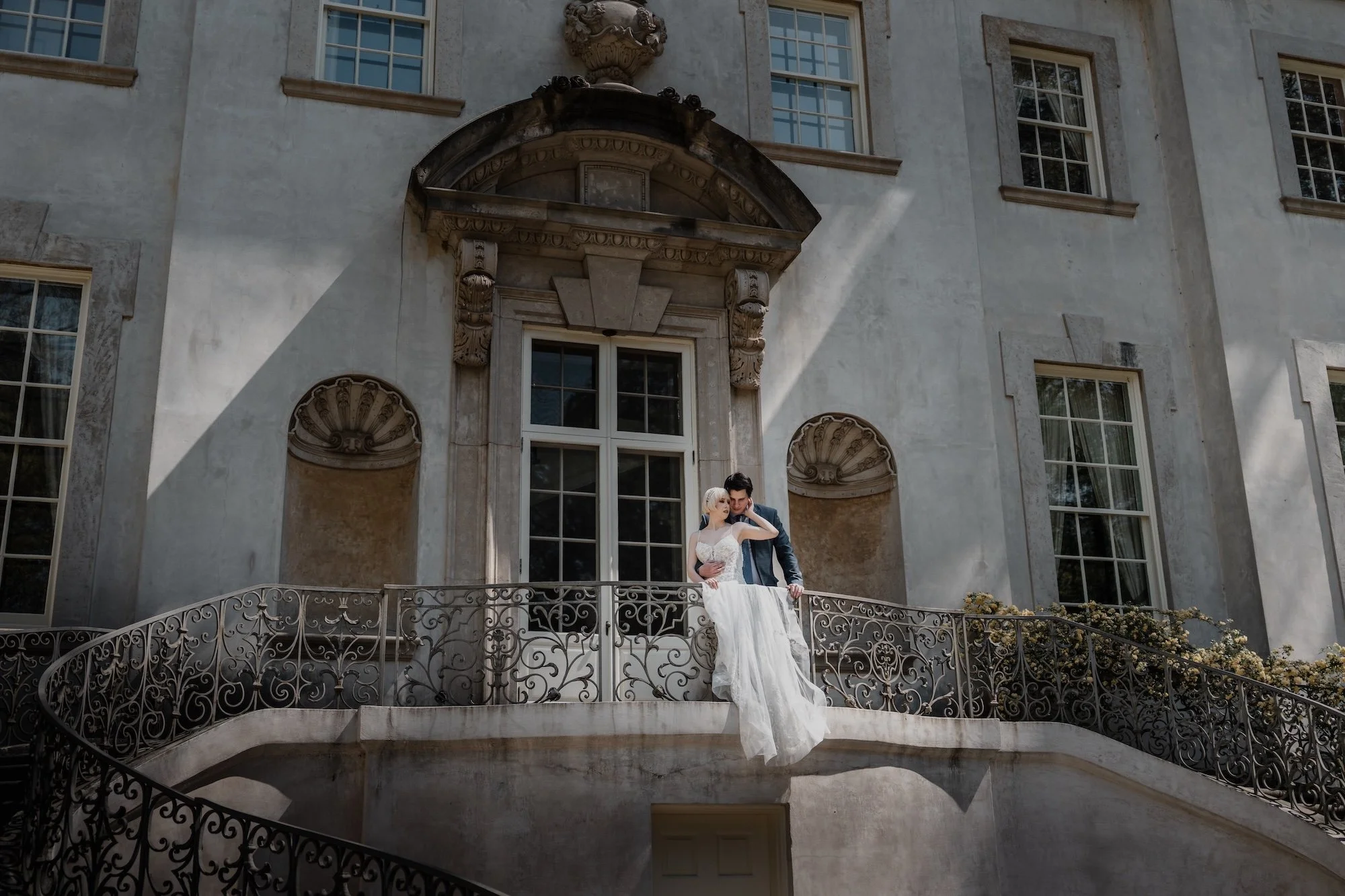 A bride pausing at the steps of a grand doorway, her veil caught in motion by the wind.