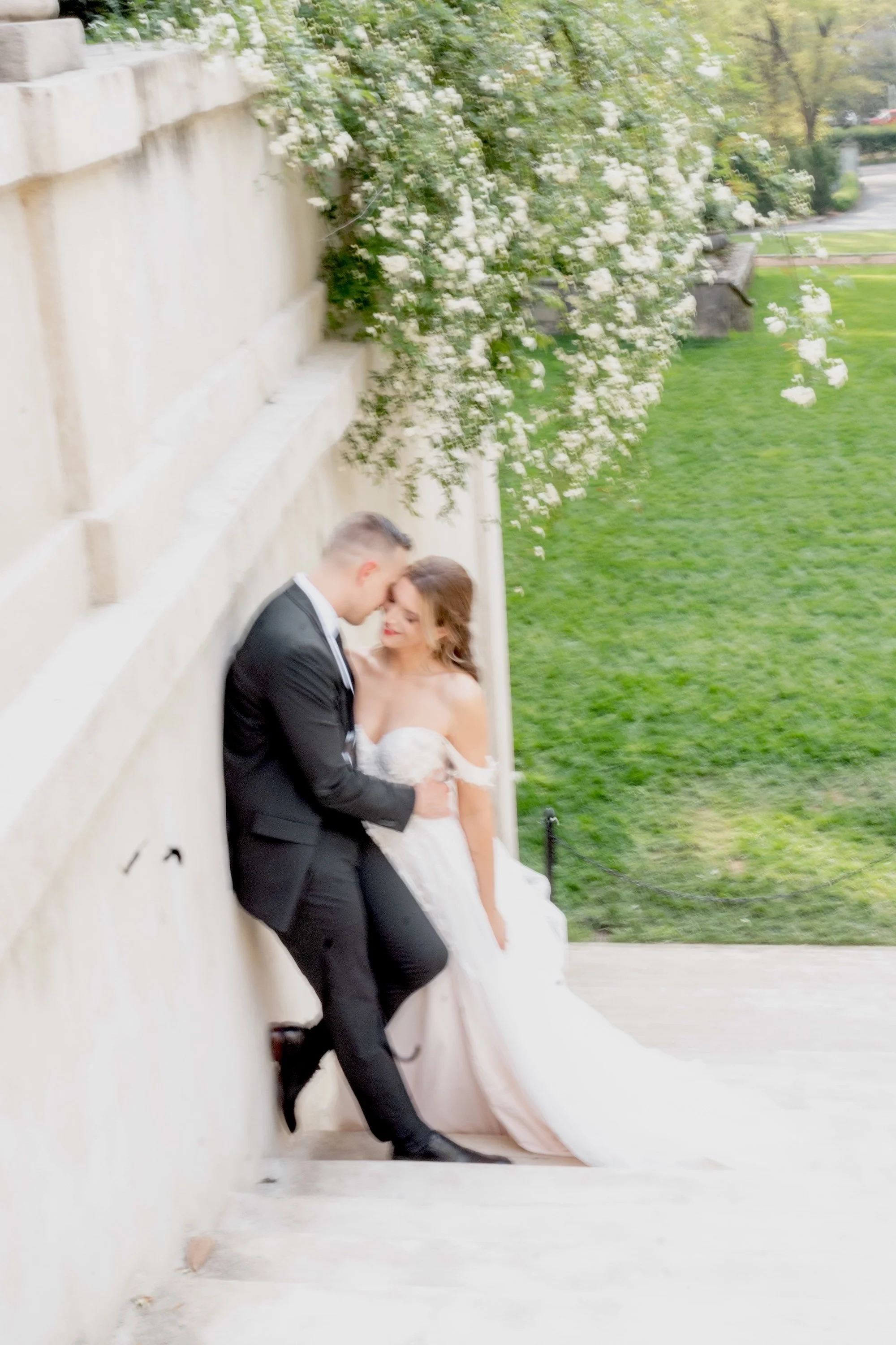 A couple leans against stone steps, kissing under a canopy of green.