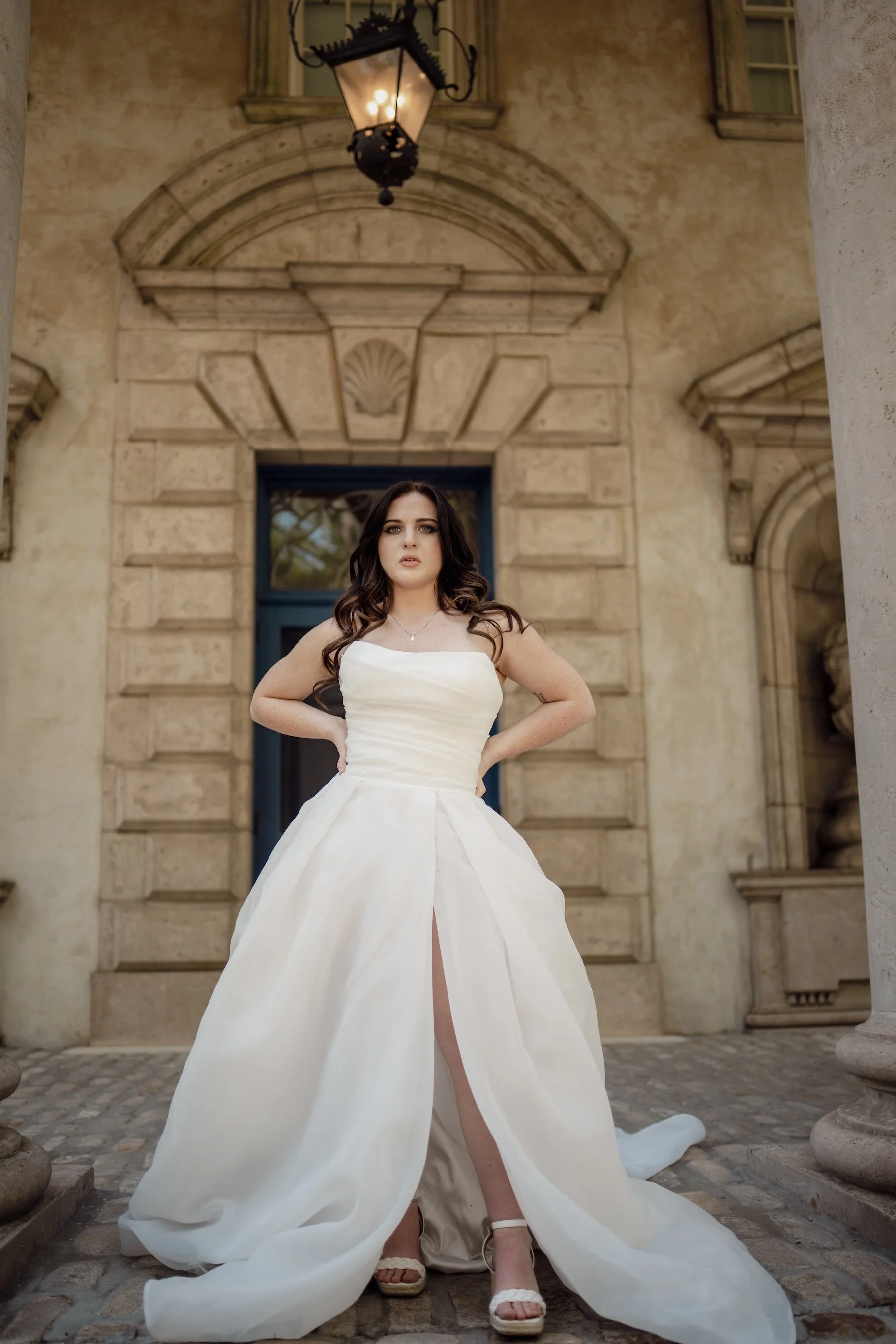 A bride stands with elegance in her gown, posture poised, the light catching the texture of fabric in timeless detail.