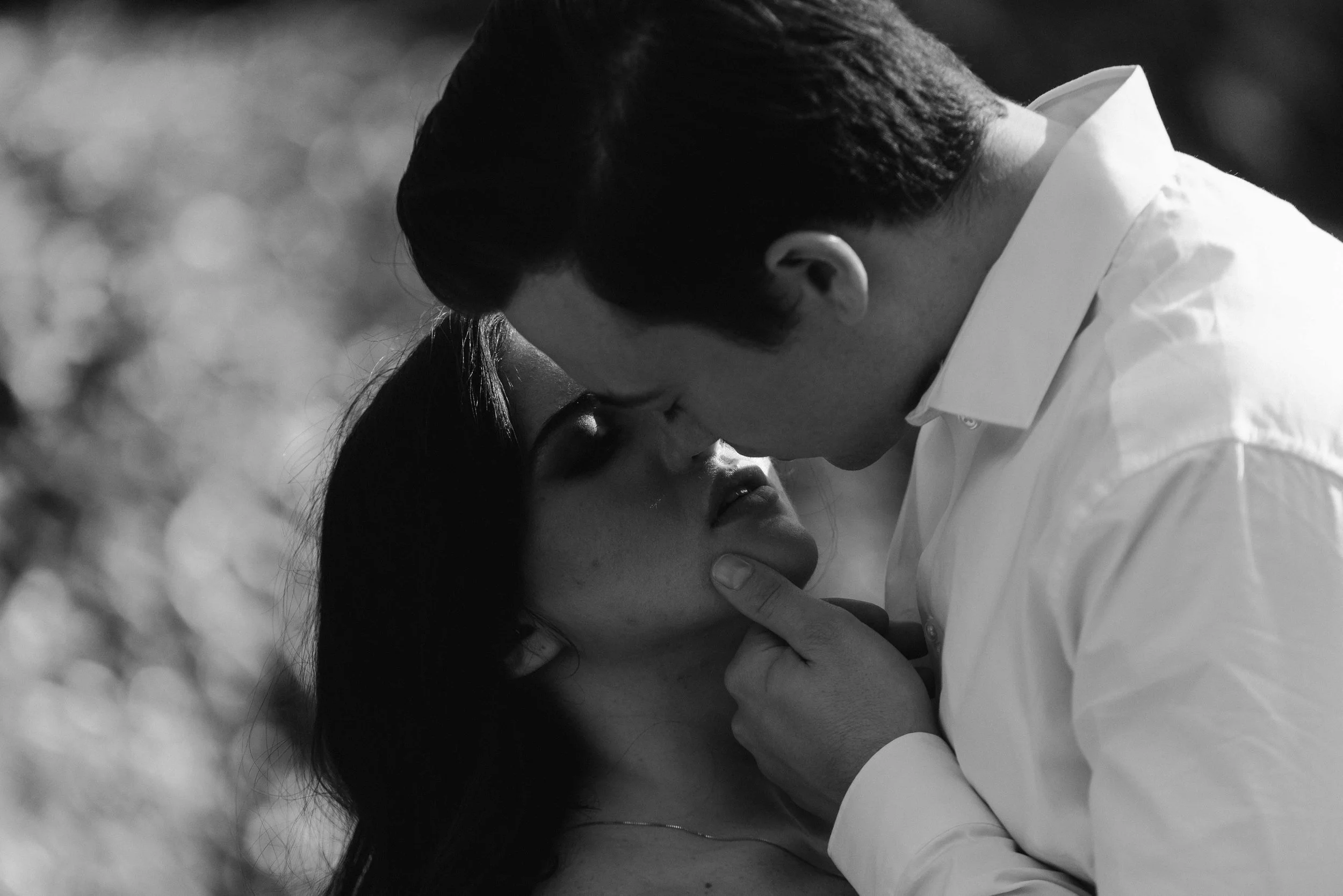 A man gently holds a woman’s face as they stand close together, their expressions framed tightly in a Fragmented Memories prenup photographer still.