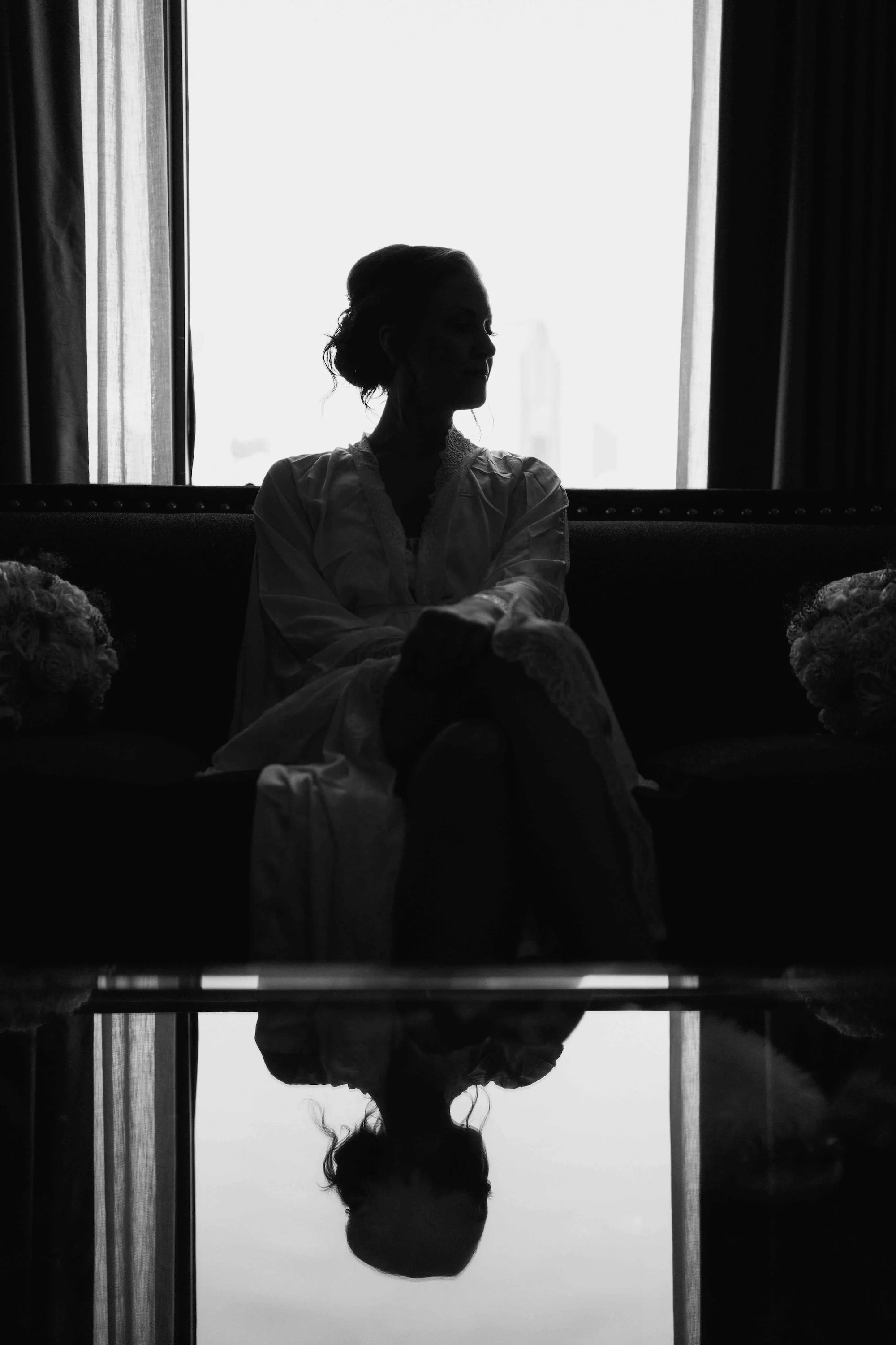 Bride seated in her gown, quiet and reflective moment framed by delicate sheer fabric.