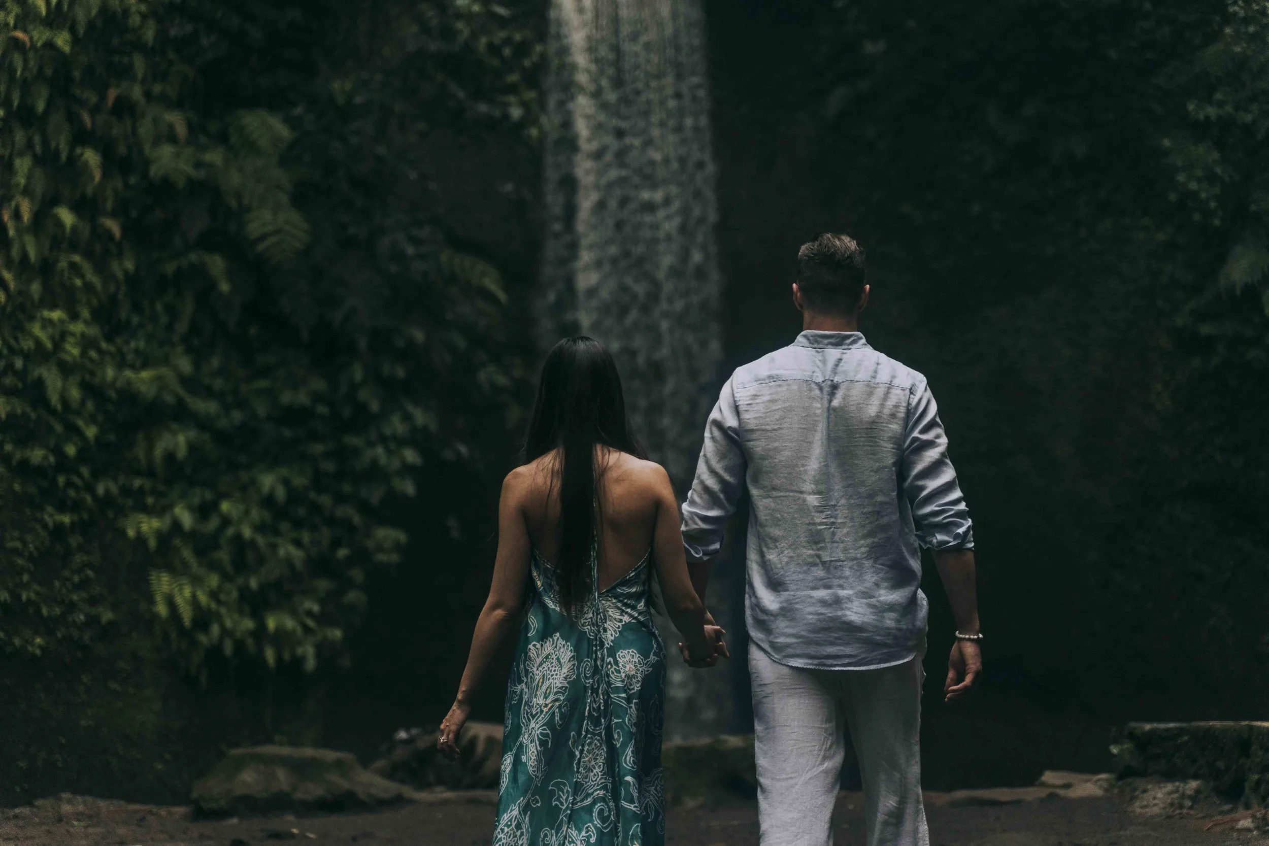 A couple walks away hand in hand toward dense greenery, observed from behind by a Fragmented Memories prenup photographer as the scene resolves.