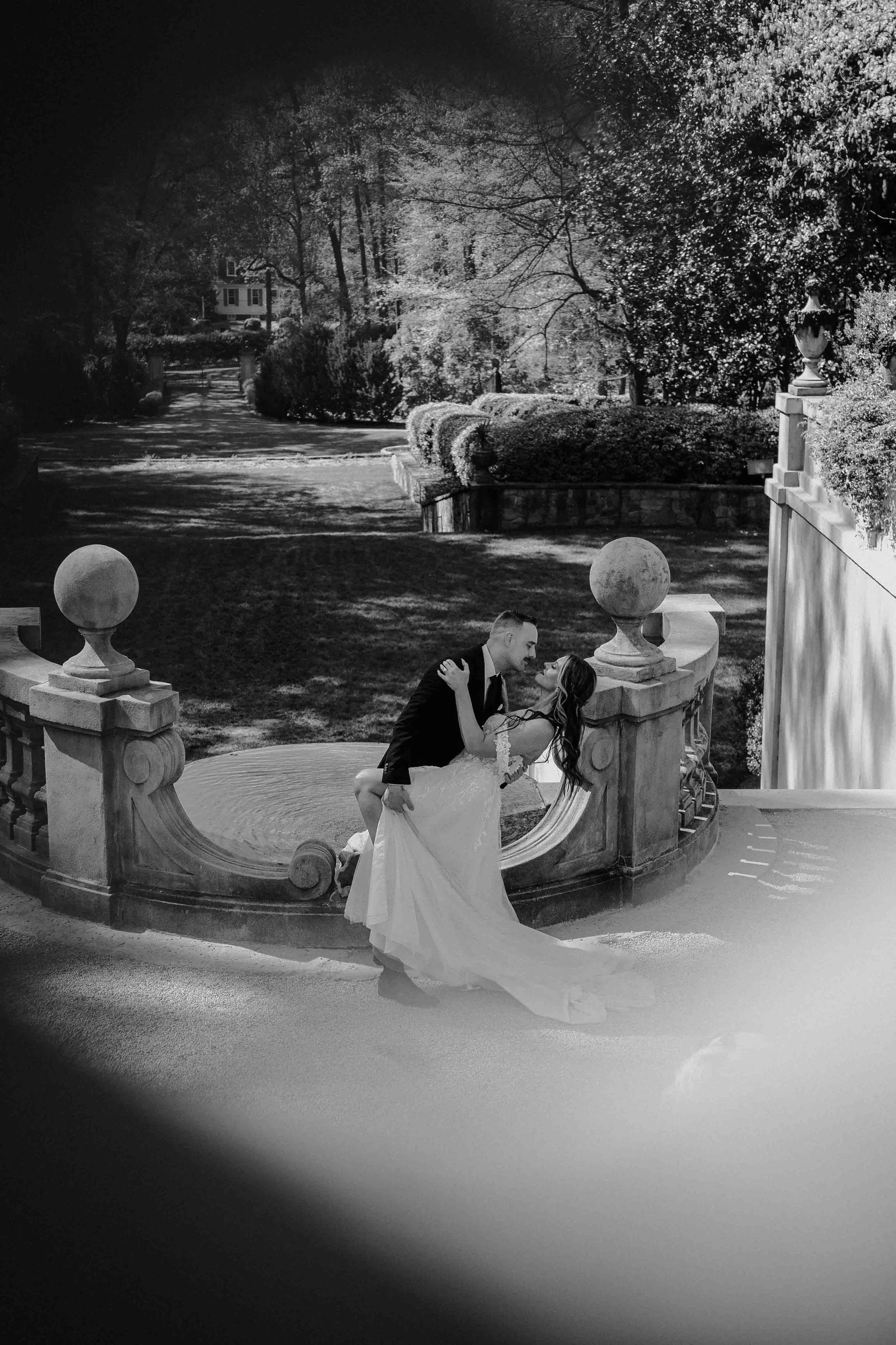 Couple shares a kiss on stone steps surrounded by gardens, timeless and elegant