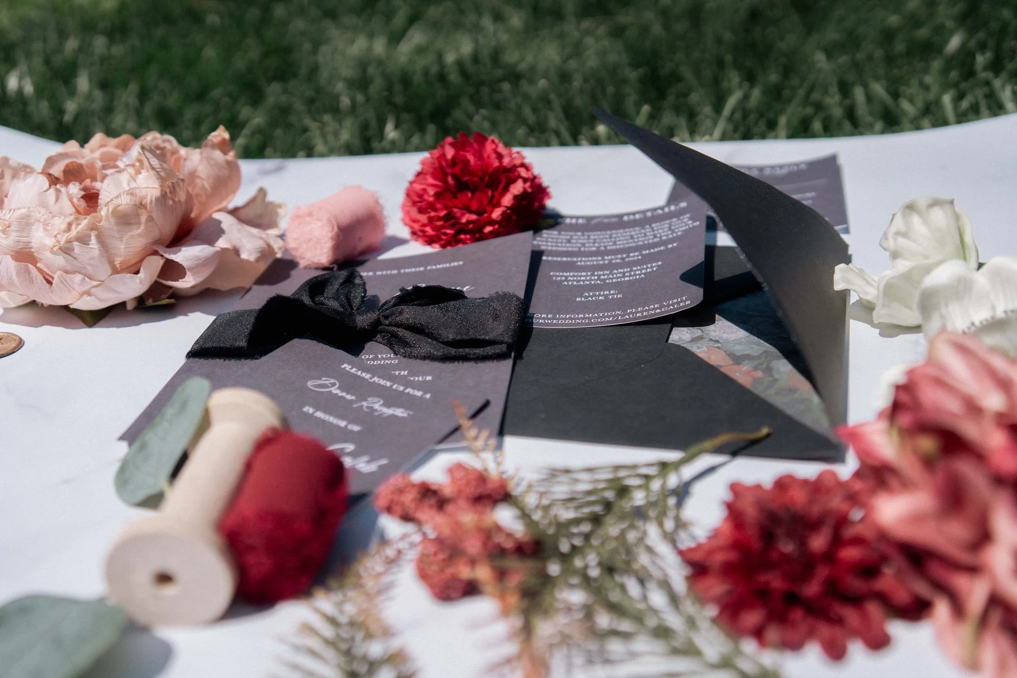 Flatlay of wedding stationery and red florals arranged on linen, styled detail photograph