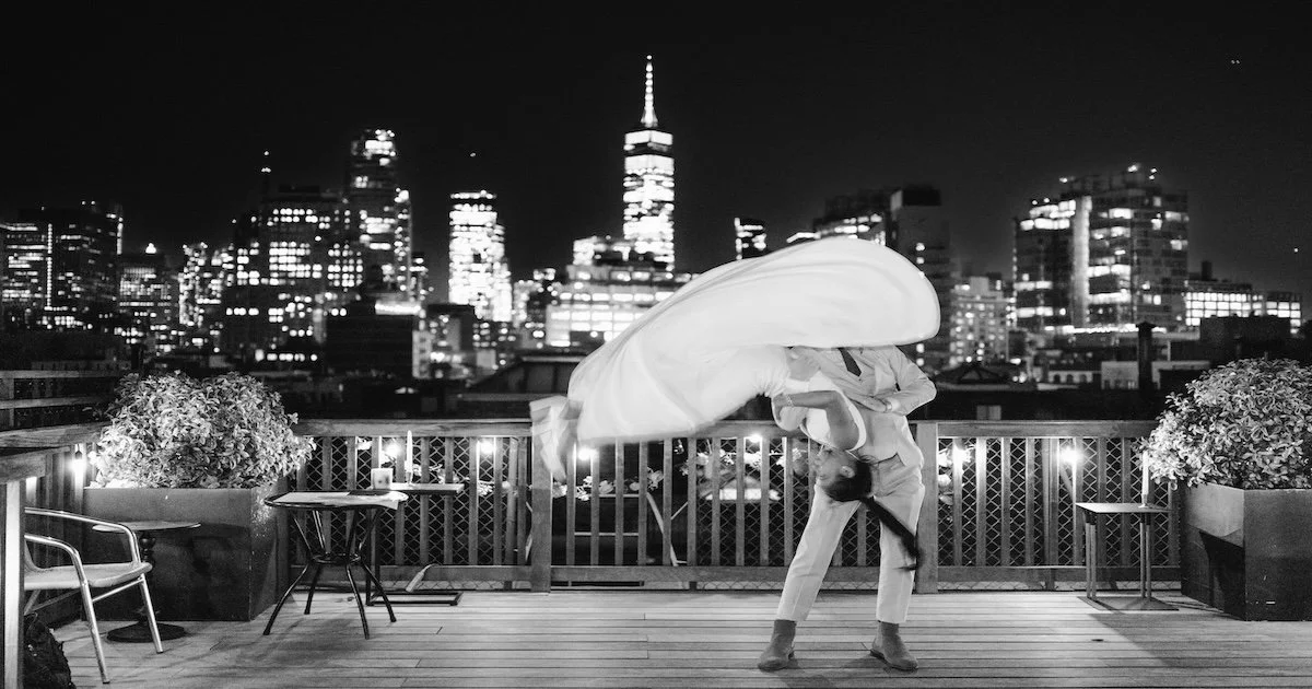A man lifts a woman into the air on a rooftop terrace, her dress suspended mid-motion like a cinematic prenup film frame.