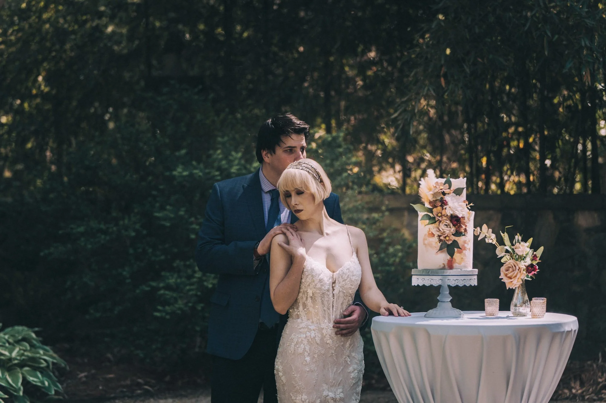 Bride playfully holds fork beside wedding cake while groom looks on, candid laughter in a garden moment, cinematic storytelling