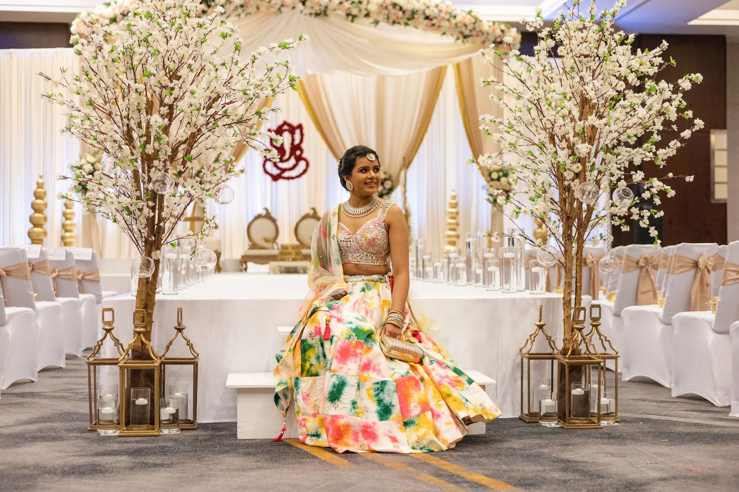 Bride in colorful lehenga seated among floral décor and candlelit lanterns, photographed in editorial style by India Wedding Photographer Caz Isaiah