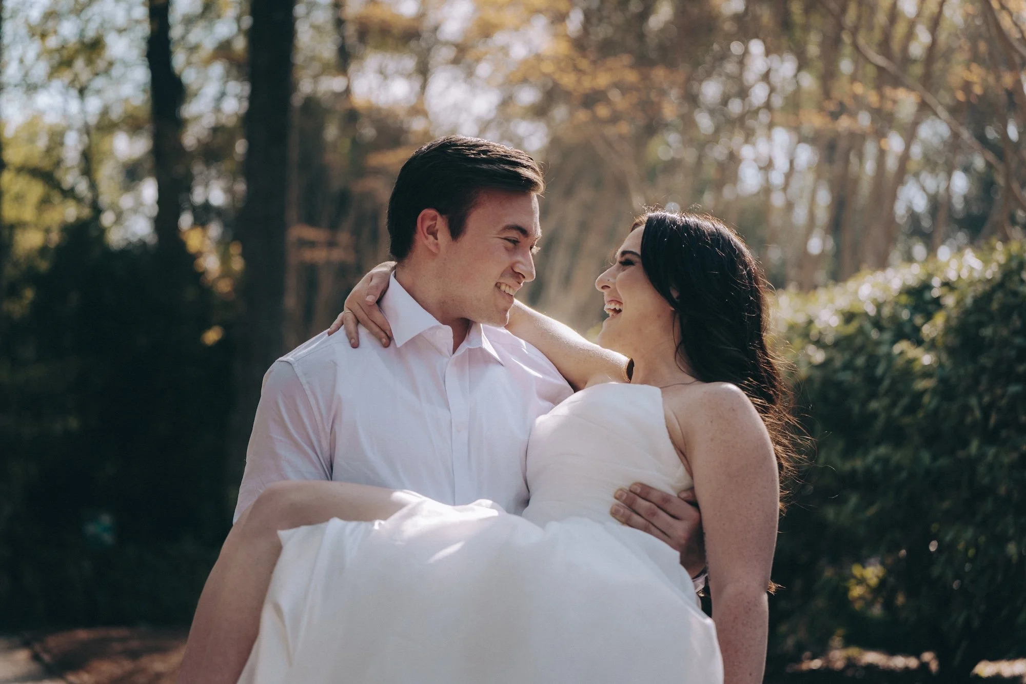 Natural and tender moment — groom carrying his bride across golden afternoon light.