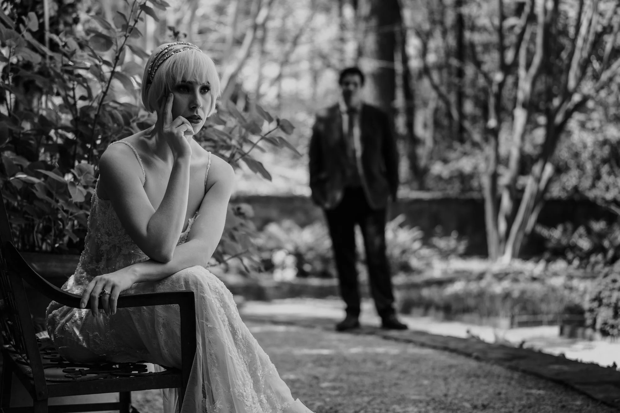 The bride sits in quiet reflection while her groom stands nearby in shadow — cinematic tones define the moment.