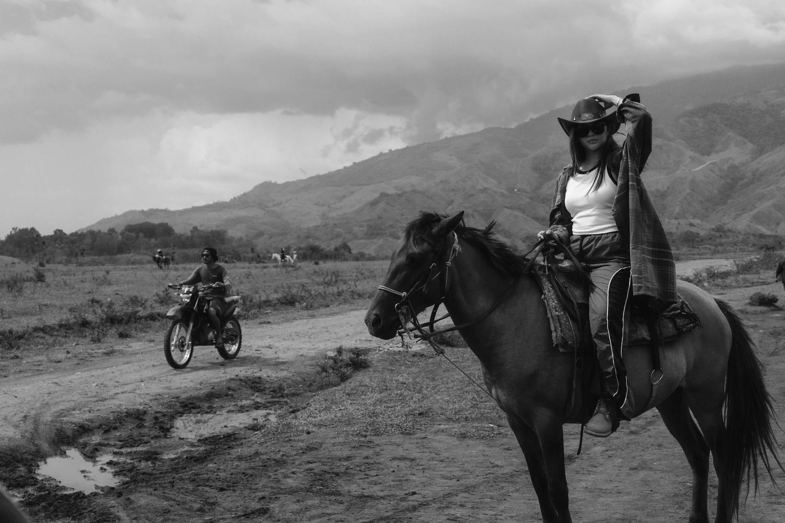 A woman sits on horseback wearing a hat as a motorcycle passes behind her on a dirt track, photographed by a Fragmented Memories couples photographer.