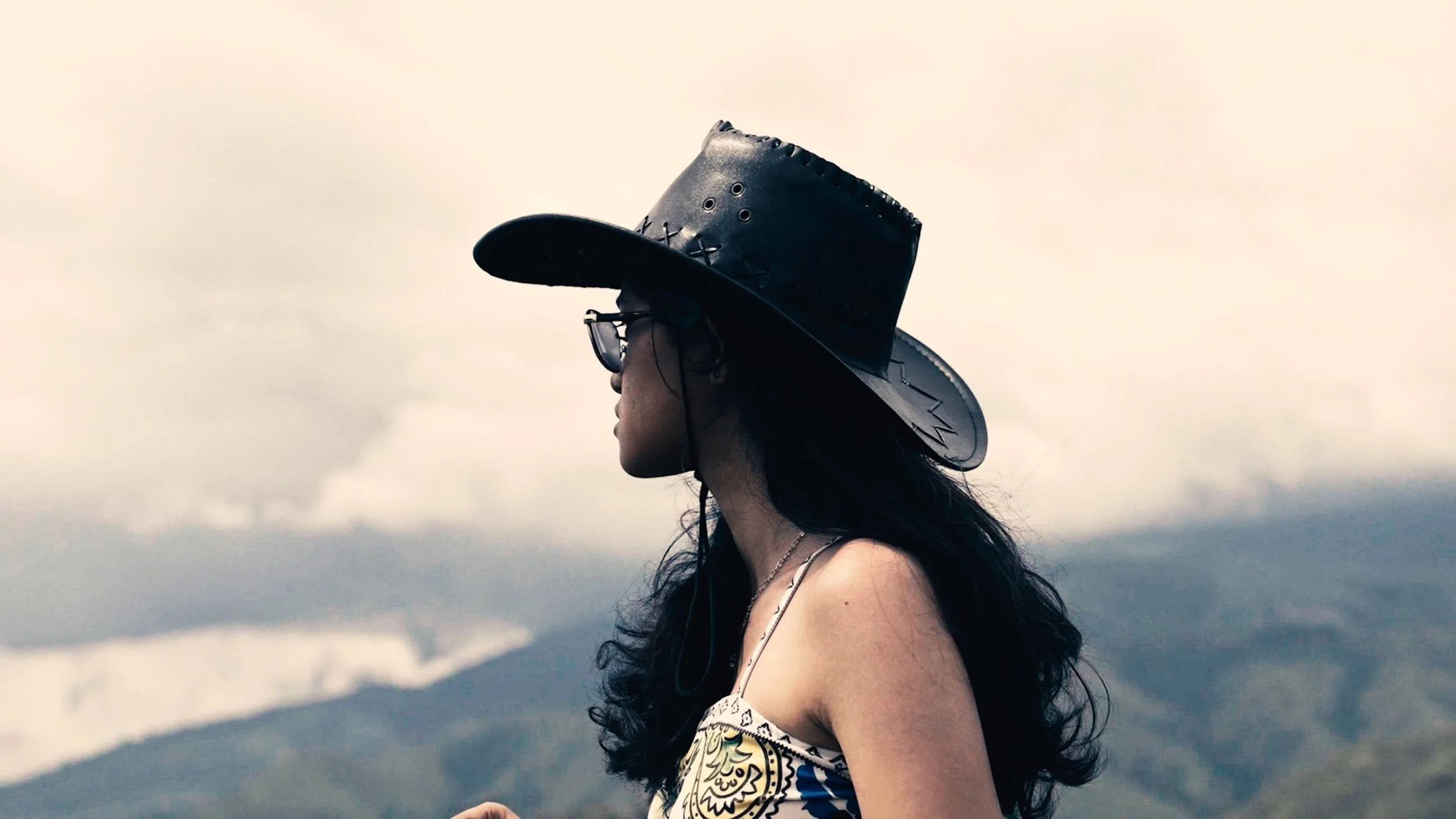 Woman in hat looking toward the horizon, styled portrait inspired by couples photography in Bali