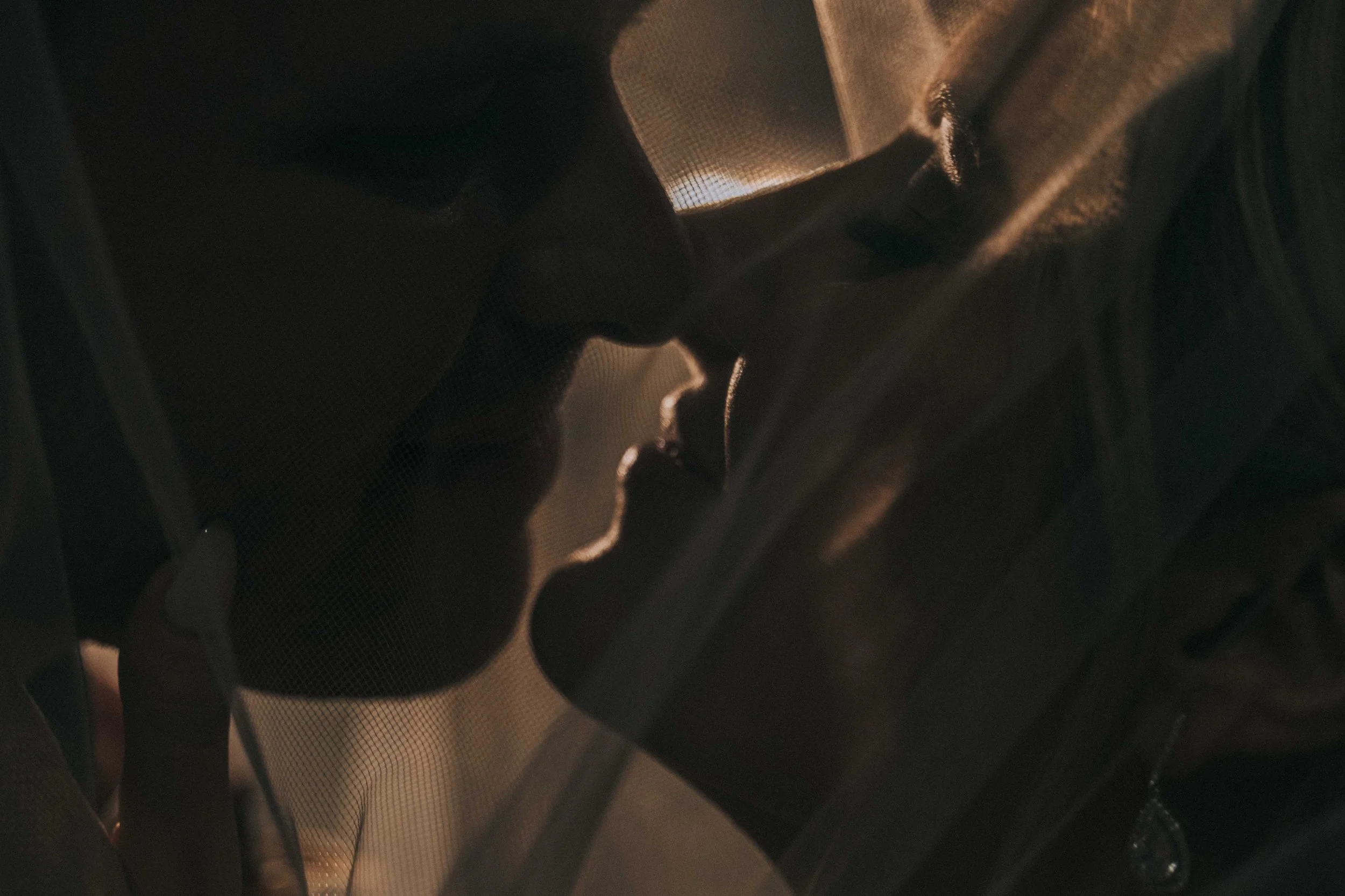 Two faces pause inches apart in soft shadow, profiles overlapping as breath and stillness settle inside a quiet cinematic frame.