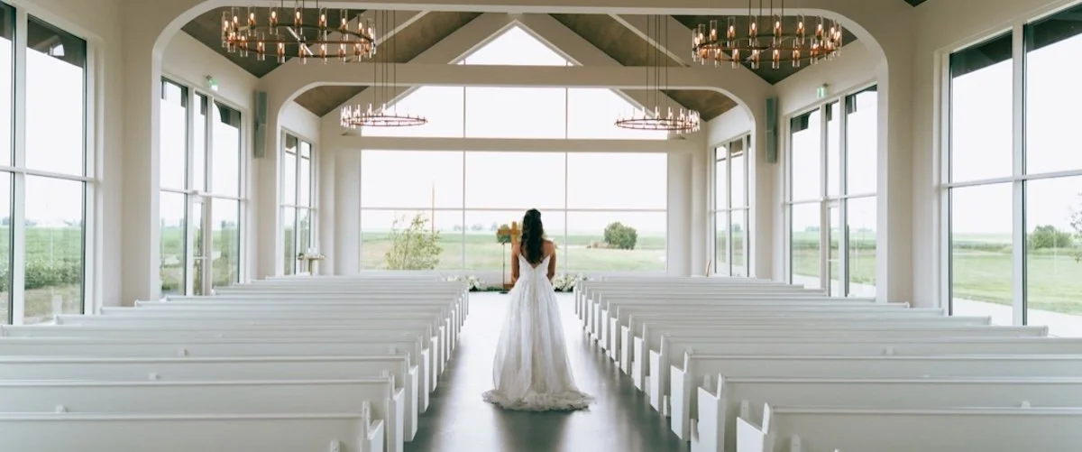 A bride walks down the aisle of a modern chapel, framed in symmetry and timeless elegance.