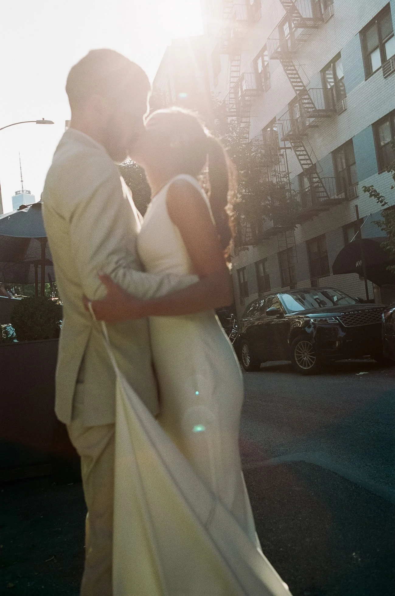 Bride and groom embrace on a quiet city street, golden sunlight casting soft glow across their faces, romantic and cinematic